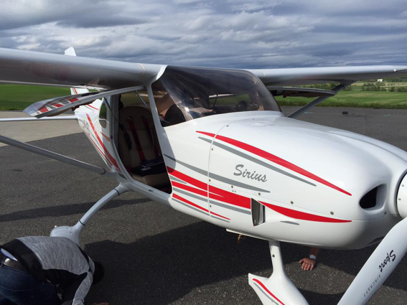 Small white aircraft with red and gray stripes parked on an airstrip under cloudy skies