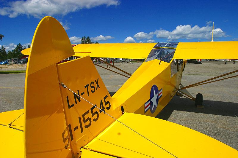Yellow vintage biplane with U.S. Air Force insignia on the fuselage, parked on an airport tarmac under a partly cloudy sky.