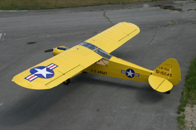 Yellow model airplane with U.S. Army and military insignia painted on it, parked on a paved surface.