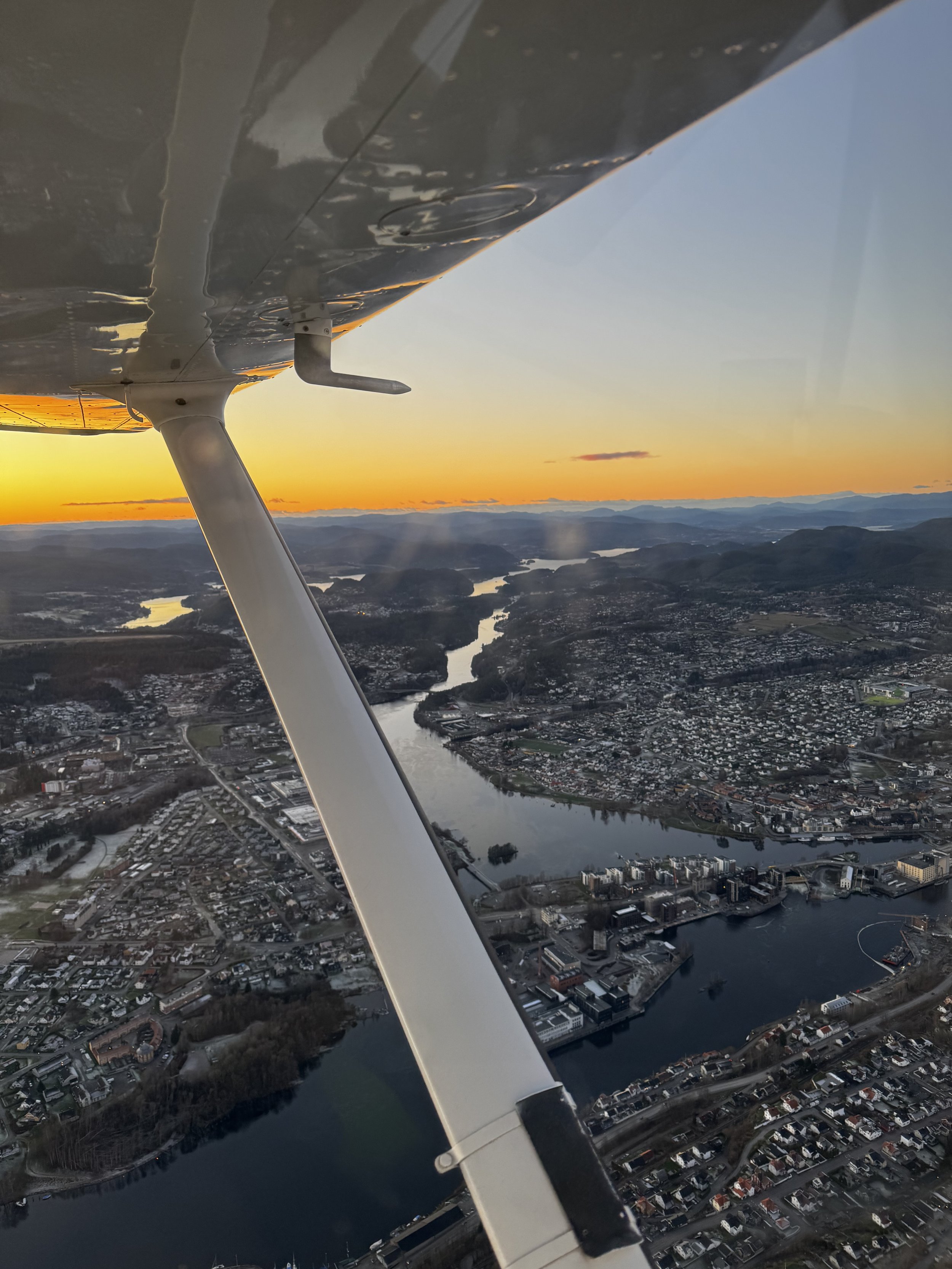 Aerial view taken from a small airplane showing a cityscape with a river winding through the city during sunset.