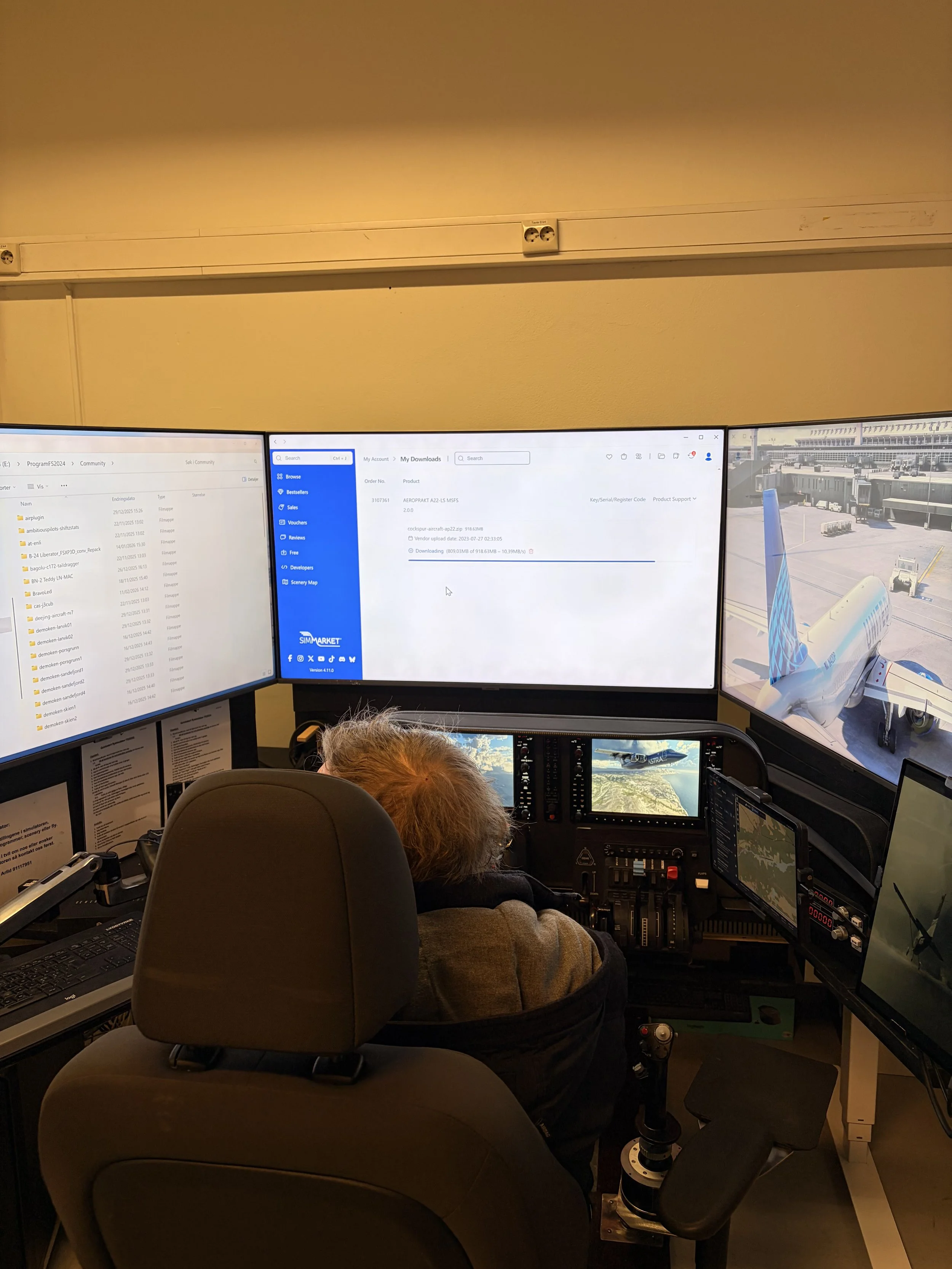 An airline pilot operating a flight simulator with three large screens. The left screen shows files and folders, the middle screen shows a download page, and the right screen displays an airplane at the airport. The pilot is seated, facing away from the camera, wearing a gray jacket.