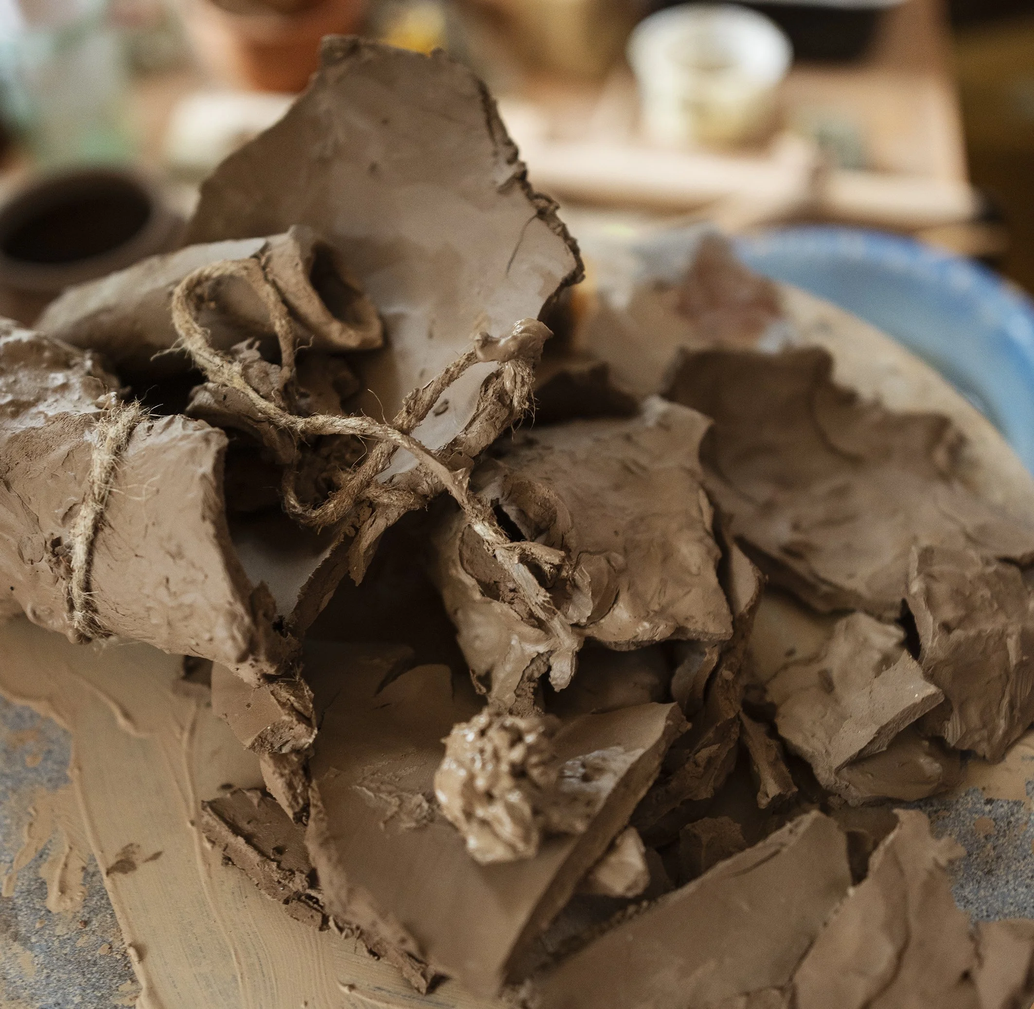 A pile of pottery shards and broken clay pieces on a pottery wheel, with a background of a workshop setting.