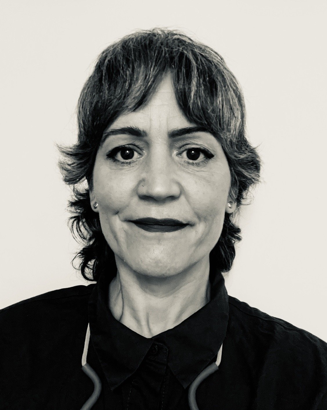 Black and white photo of a woman with short, wavy hair, wearing a dark collared shirt and a stethoscope around her neck.