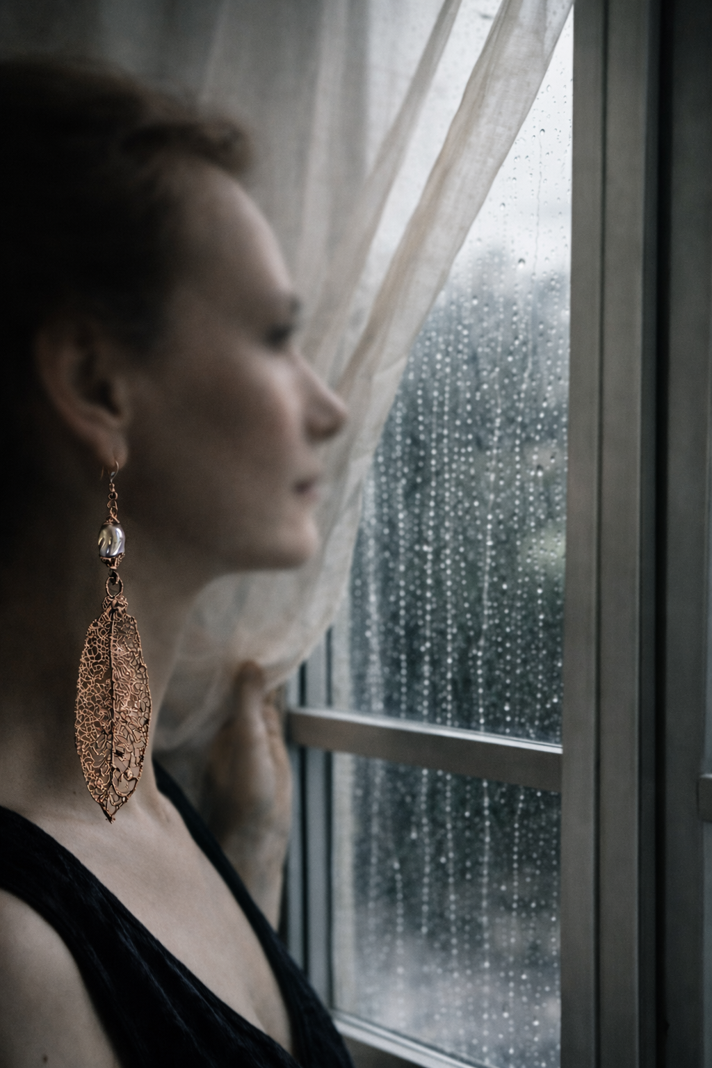 Donna che guarda fuori dalla finestra, indossa l’orecchino Limone in rame di Natasha Lume – arte indossabile