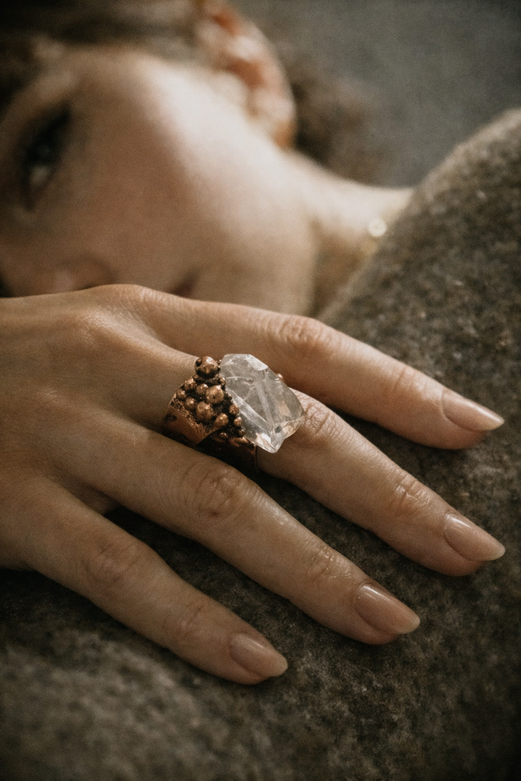 Mano con anello grande in rame, volto femminile sfocato su sfondo scuro, arte indossabile di Natasha Lume, Versilia