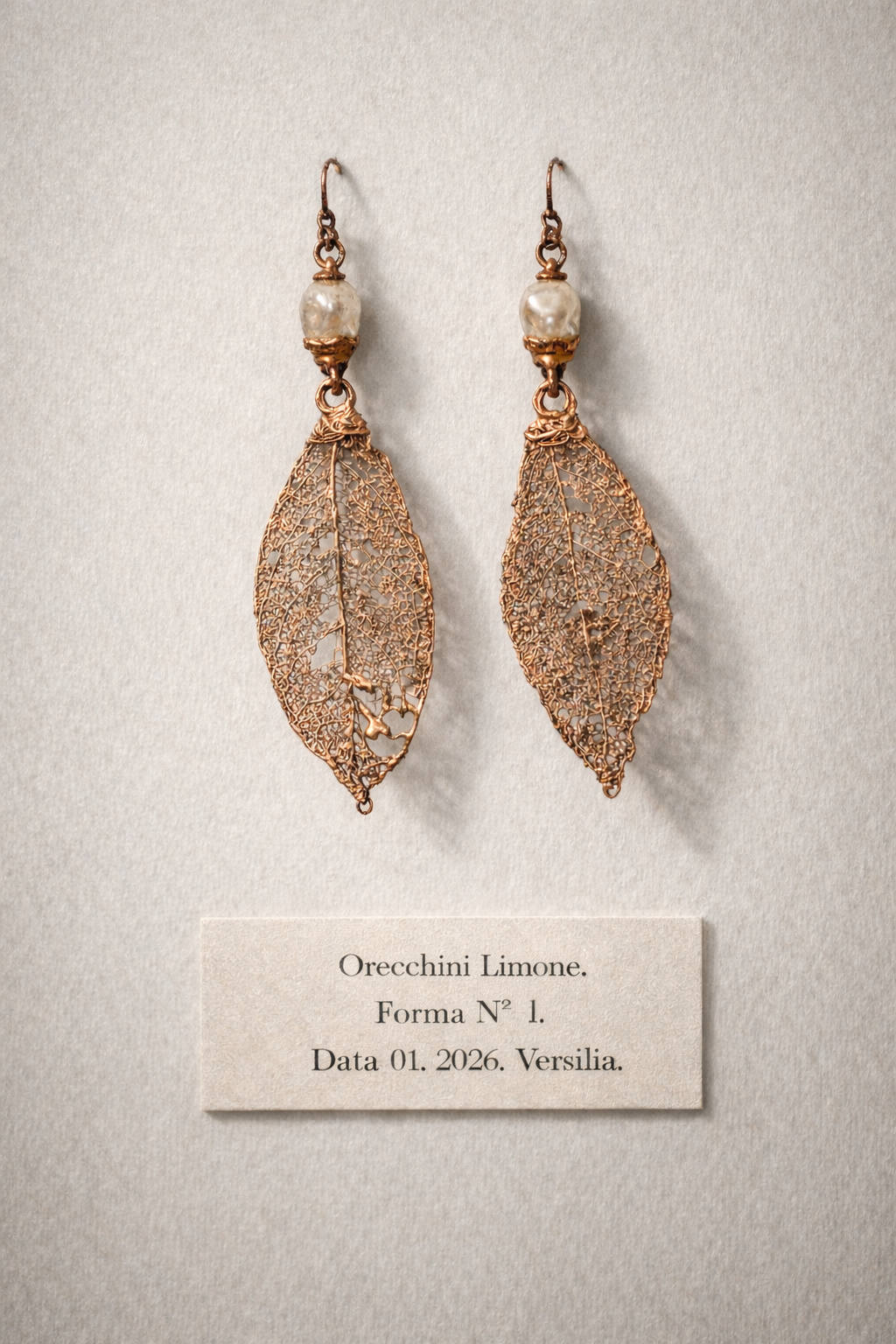 Orecchini pendenti a forma di foglia in metallo con perle bianche, arte indossabile di Natasha Lume, esposti come oggetti museali