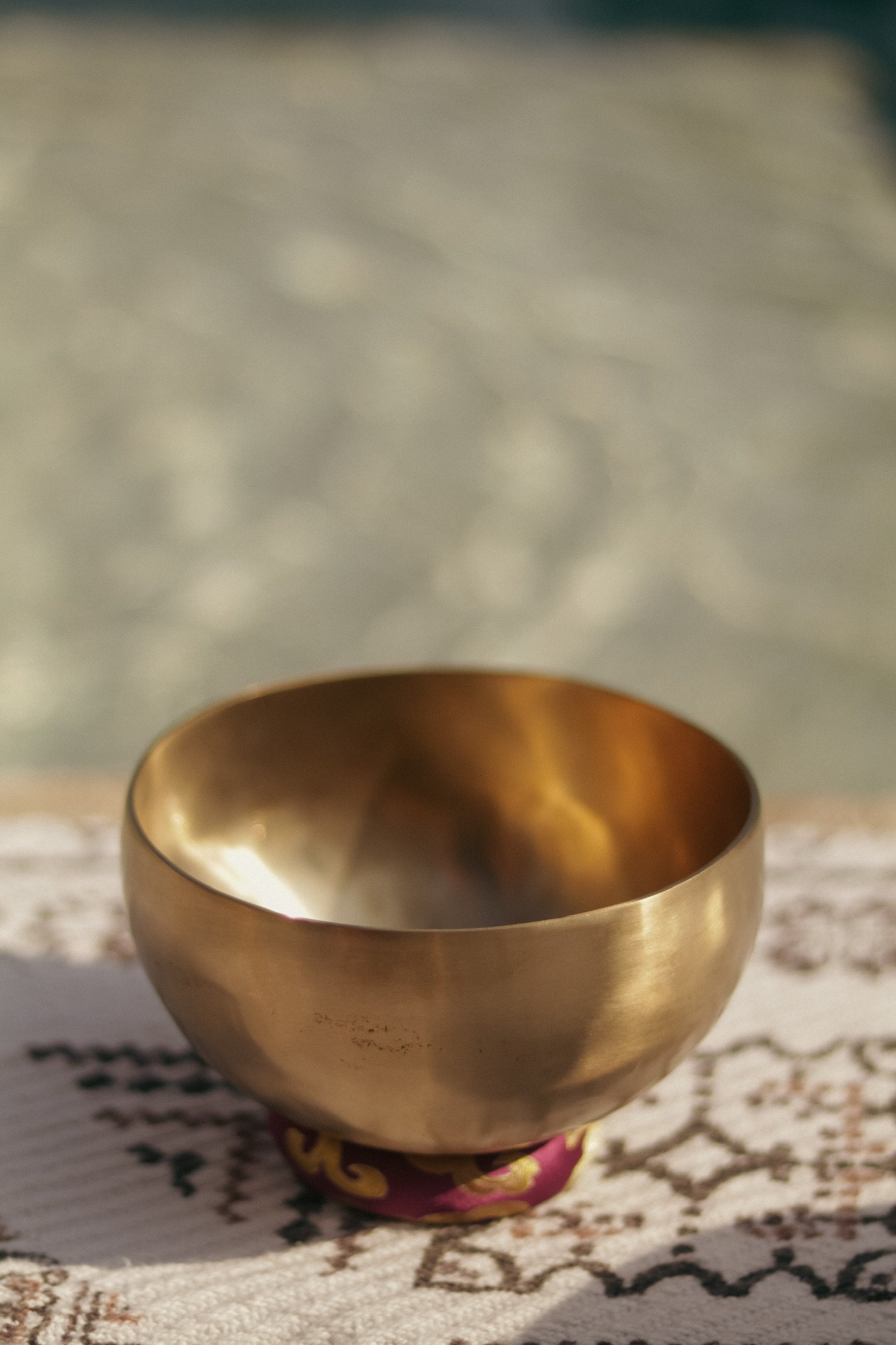 A brass singing bowl placed on a decorative cloth surface with blurred background.