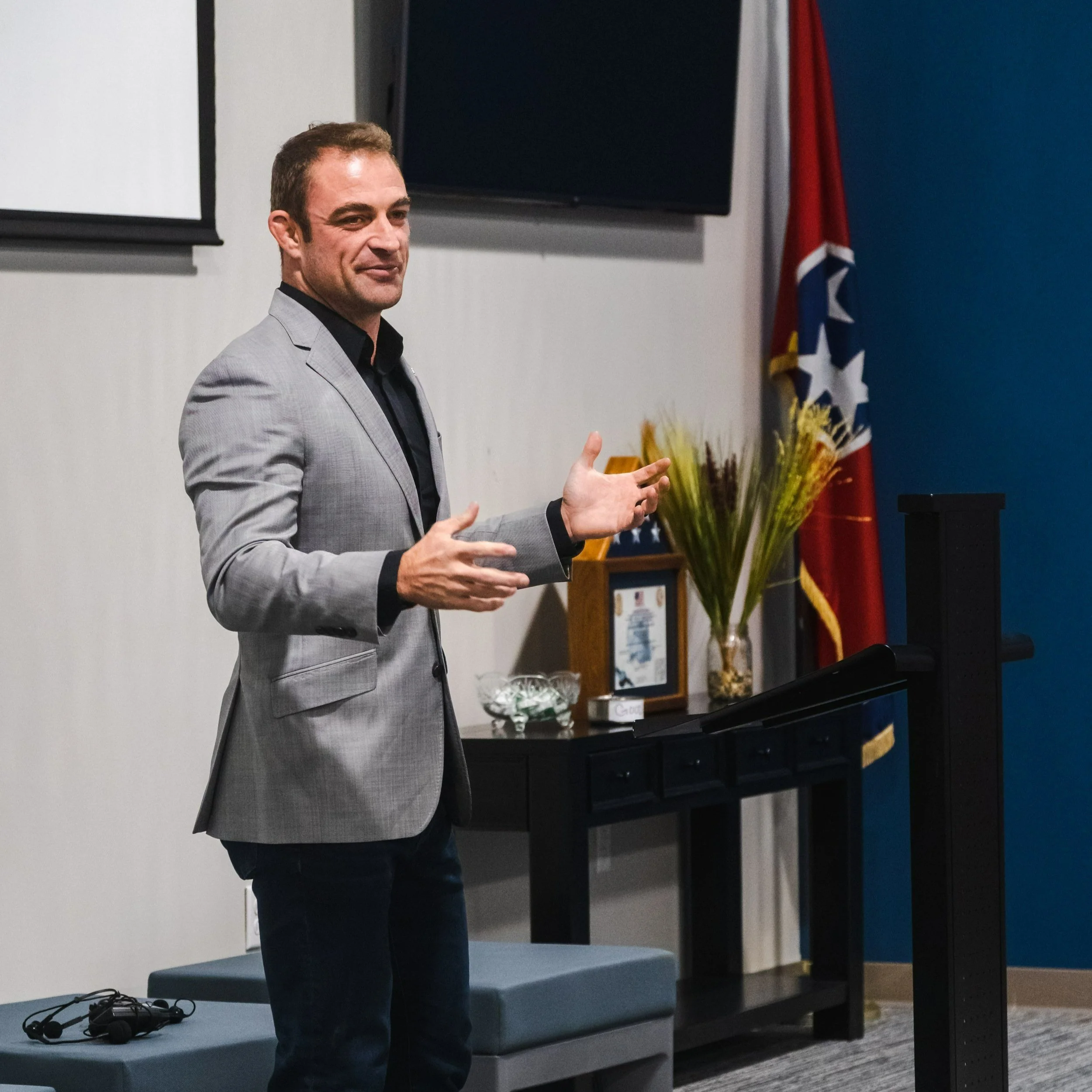 A man in a gray blazer giving a presentation in a conference room.
