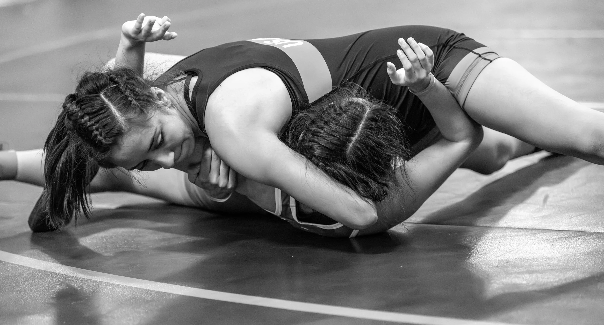 Two female wrestlers engaged in a match on a wrestling mat, with one wrestler pinning the other on the ground.