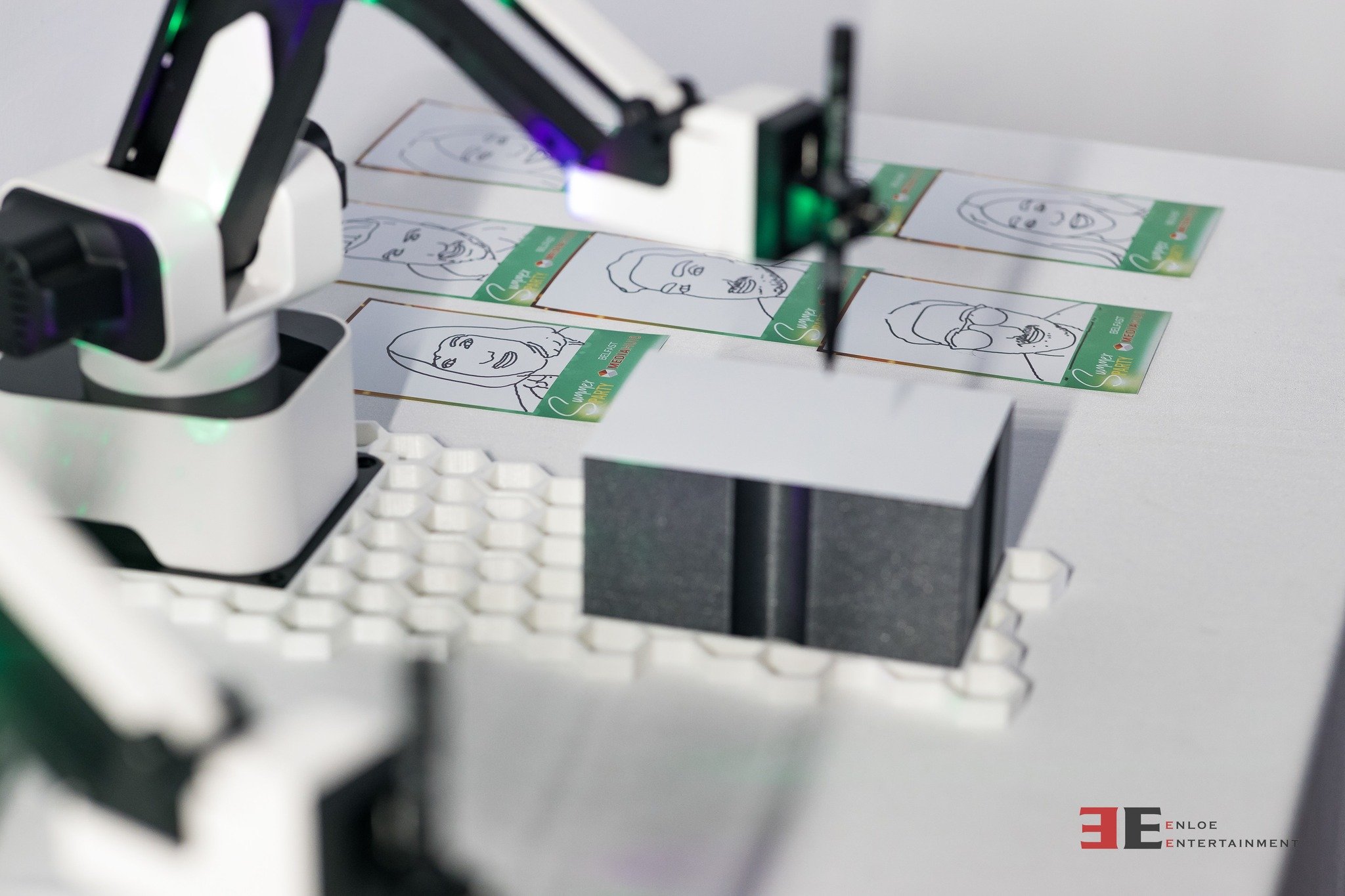 A robotic arm is printing or sorting cards with illustrated faces and text on a table.