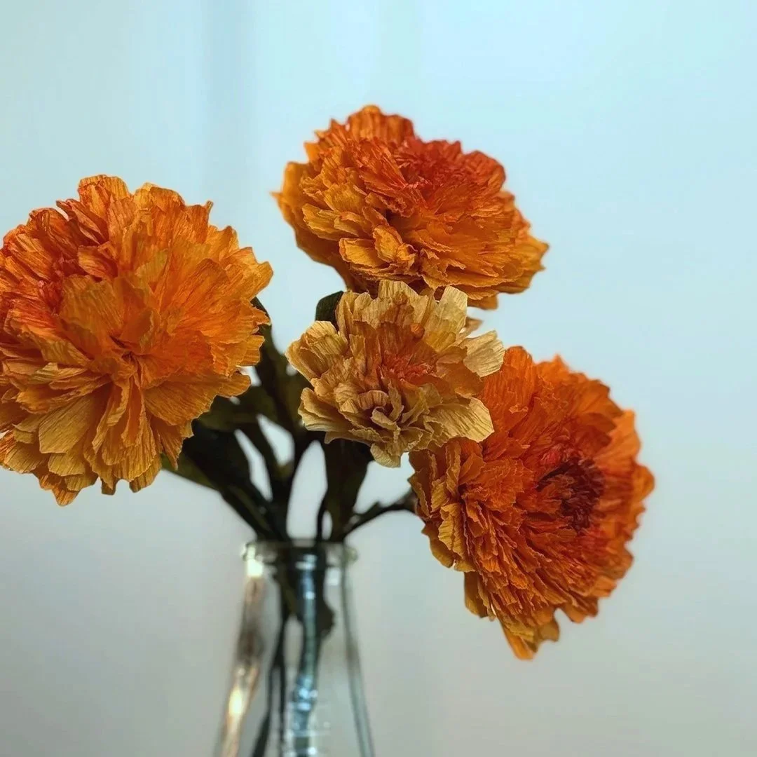 A bouquet of orange and yellow carnations in a clear glass vase against a light background.