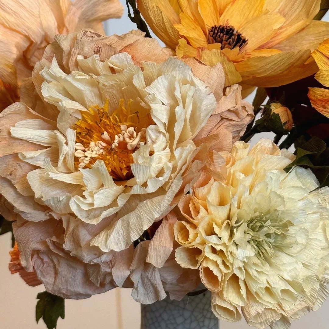 Close-up of cream-colored and peach artificial peony flowers in a vase.