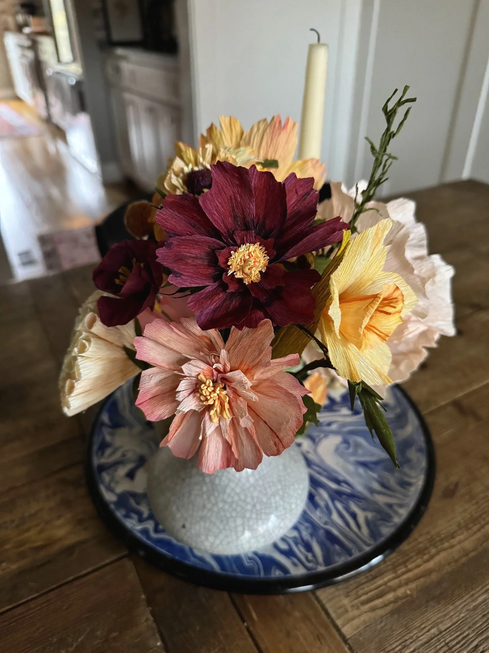 A bouquet of faux flowers in a textured white vase on a matching blue and white tray, placed on a wooden table