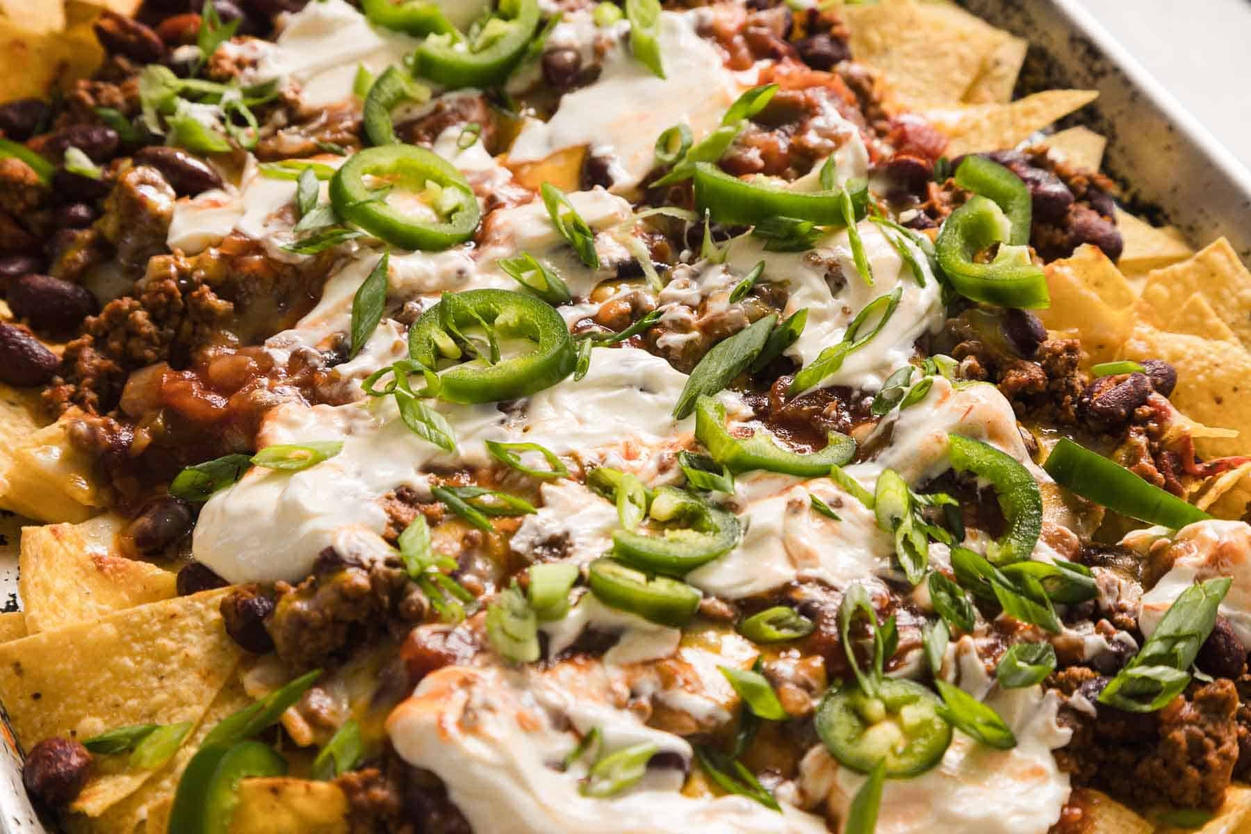 Close-up of a tray of loaded nachos topped with ground beef, black beans, sour cream, sliced green onions, and melted cheese.