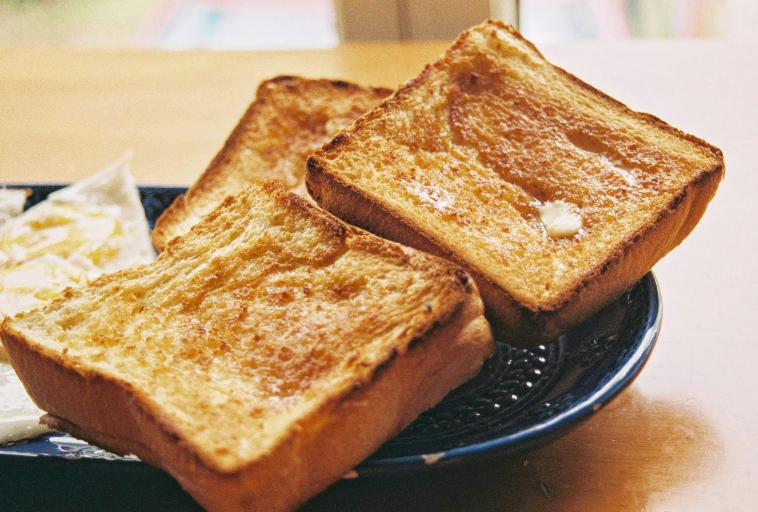 Three slices of toasted bread with butter on a dark blue plate.