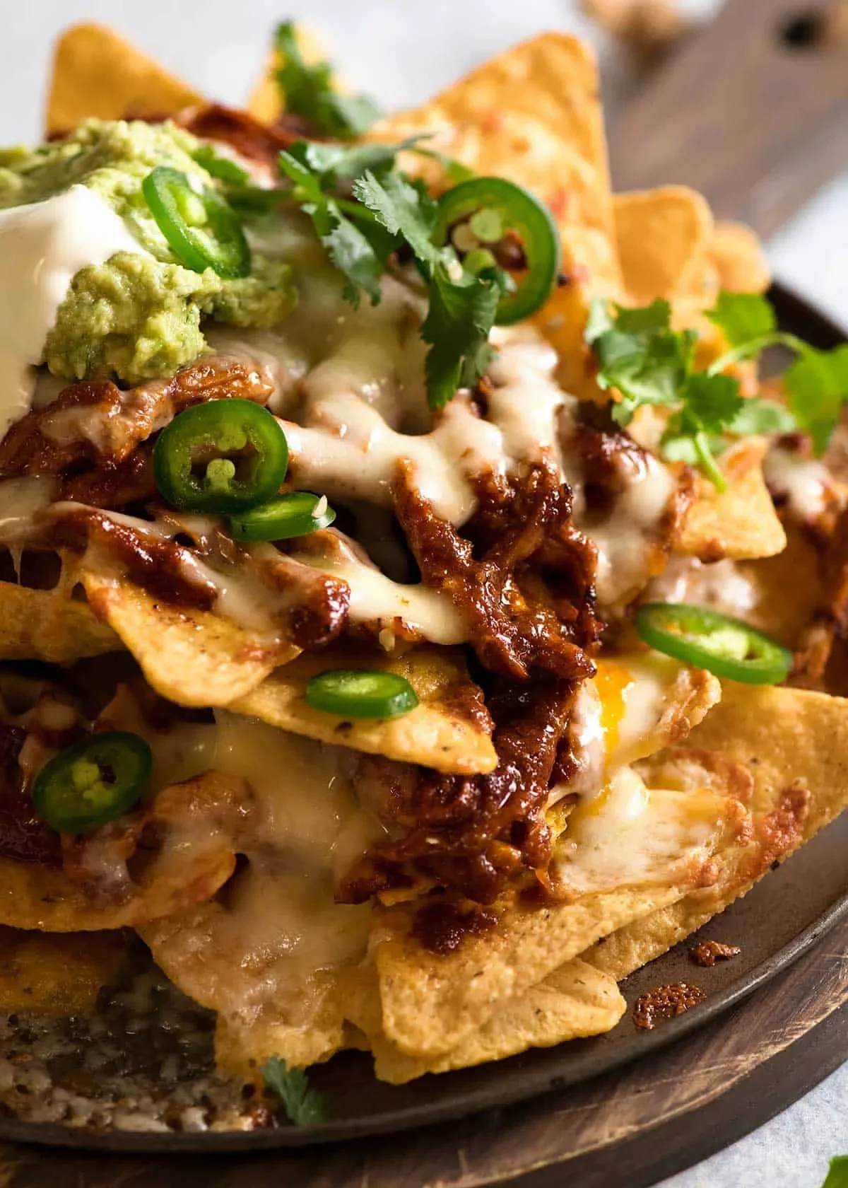 Close-up of loaded nachos topped with melted cheese, beef, jalapeño slices, guacamole, sour cream, and cilantro.