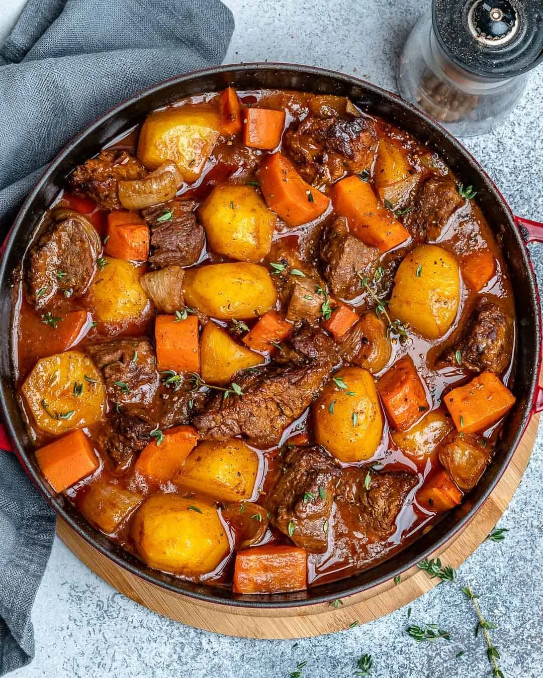 Pot roast with potatoes, carrots, and onions in a thick gravy, garnished with herbs, in a black skillet on a wooden cutting board.