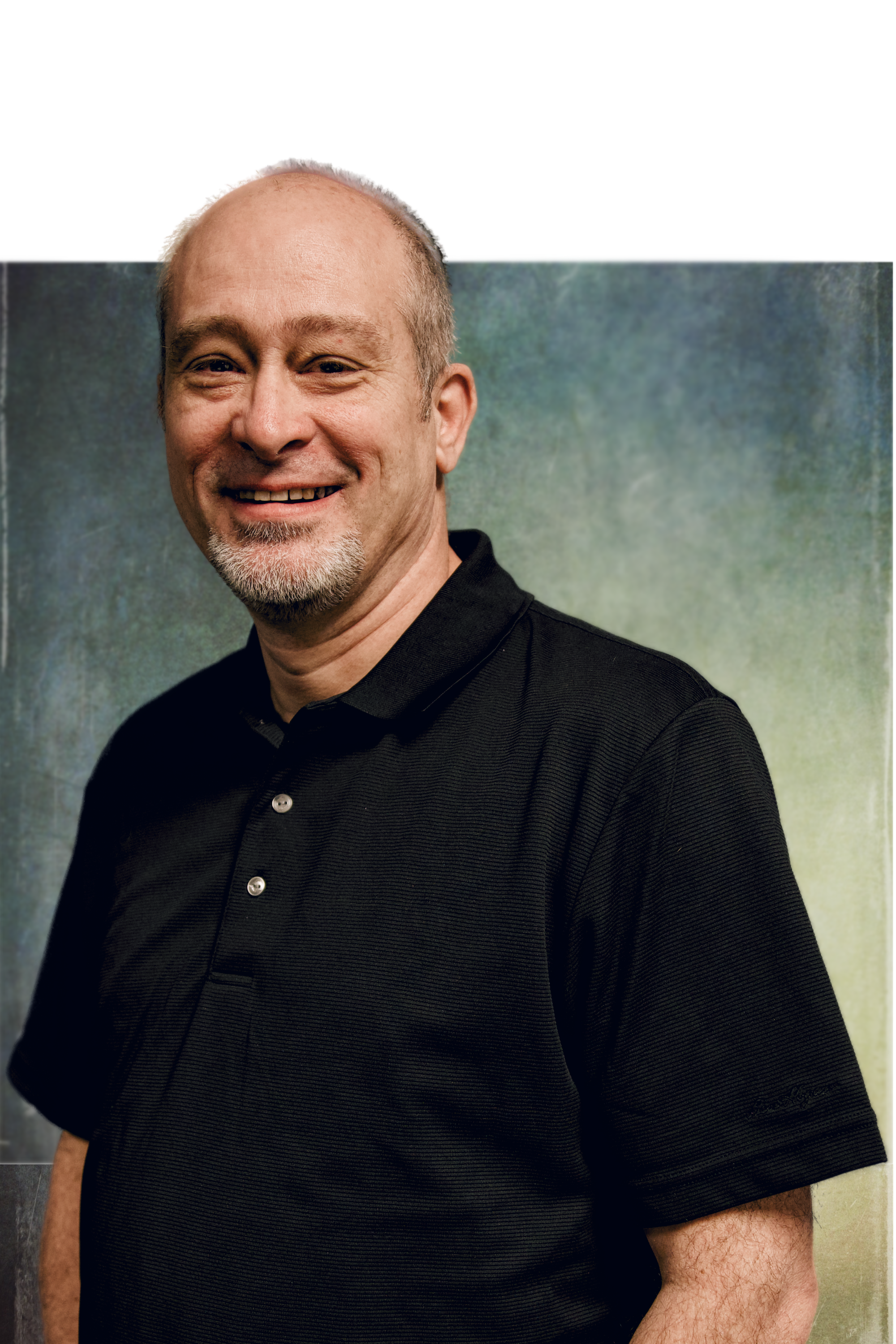 Smiling middle-aged man with short hair, goatee, wearing a black polo shirt, standing against a colorful background.