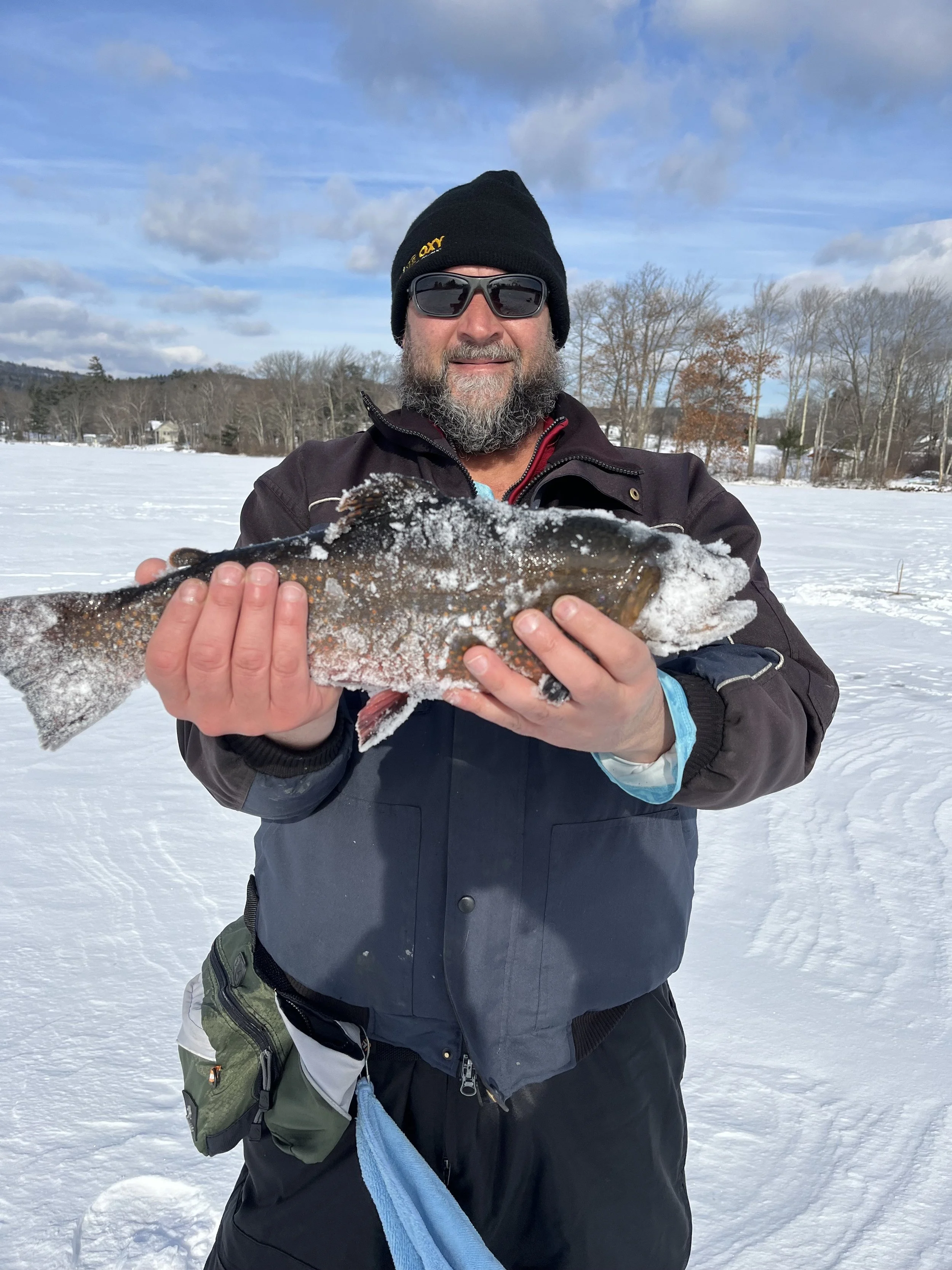 Man in winter clothes holding a large fish on a snowy outdoor ice-covered lake