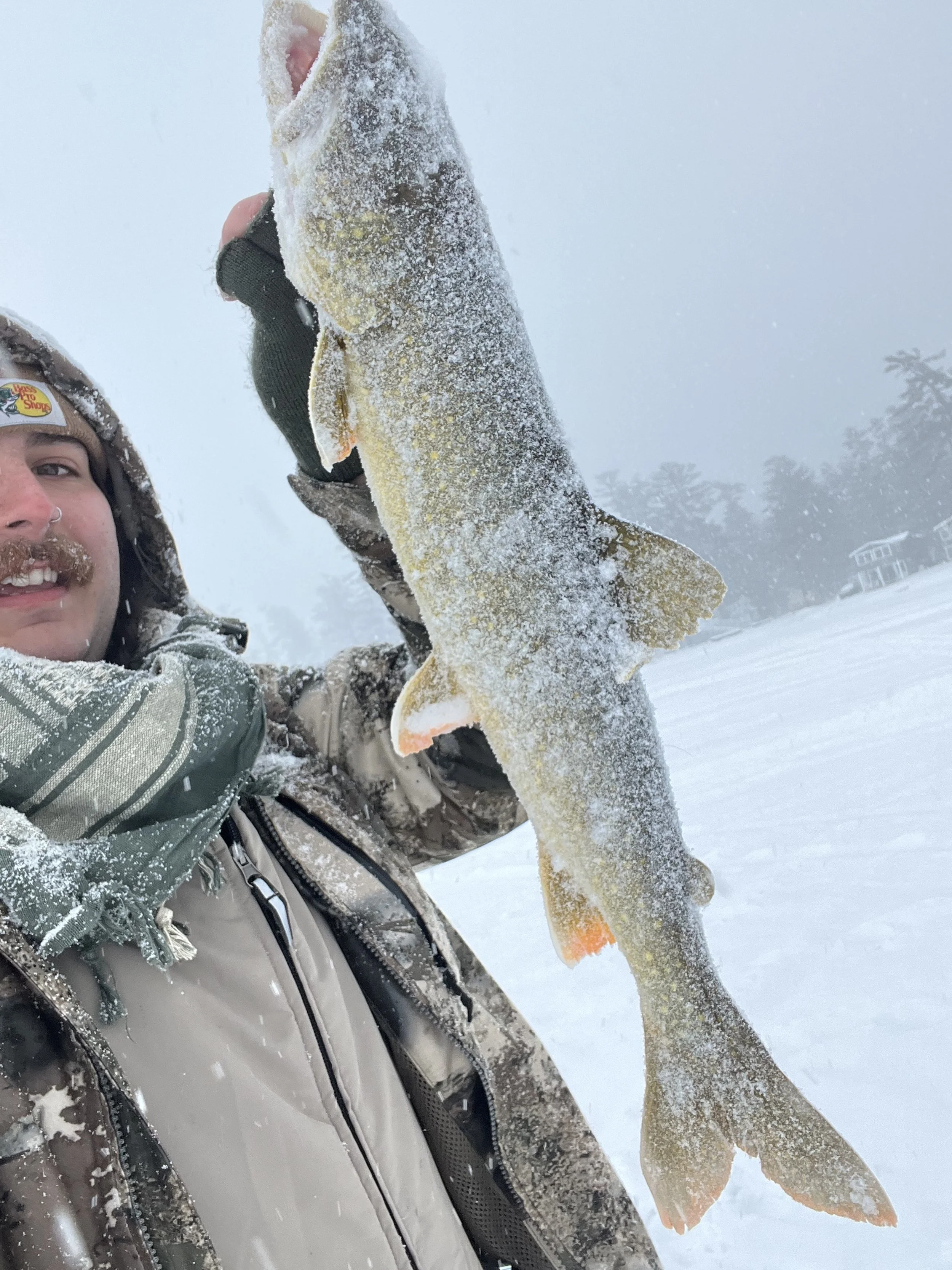 Man holding a large fish in a snowy landscape.