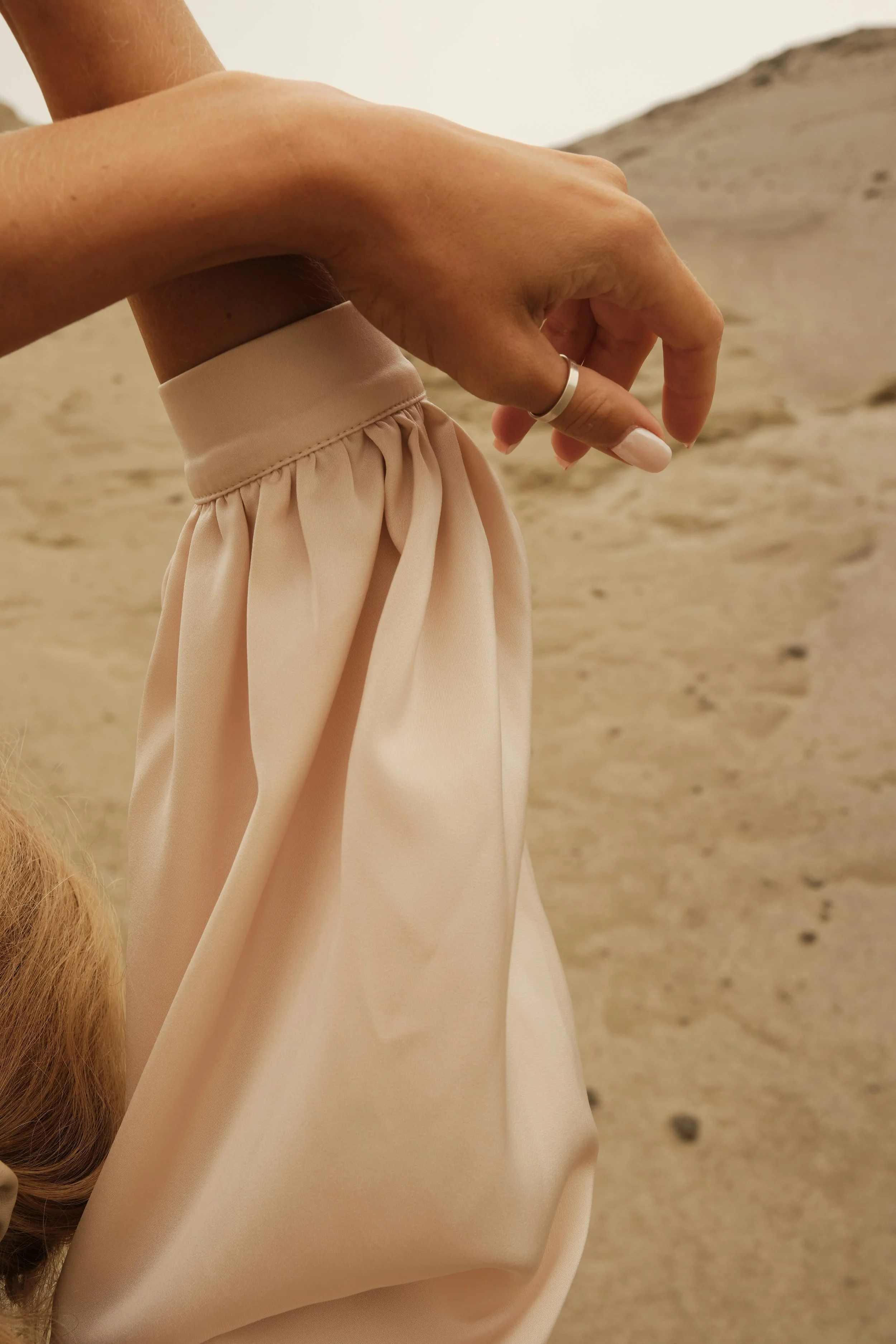 Close-up of a hand holding a piece of beige fabric against a desert-like background.