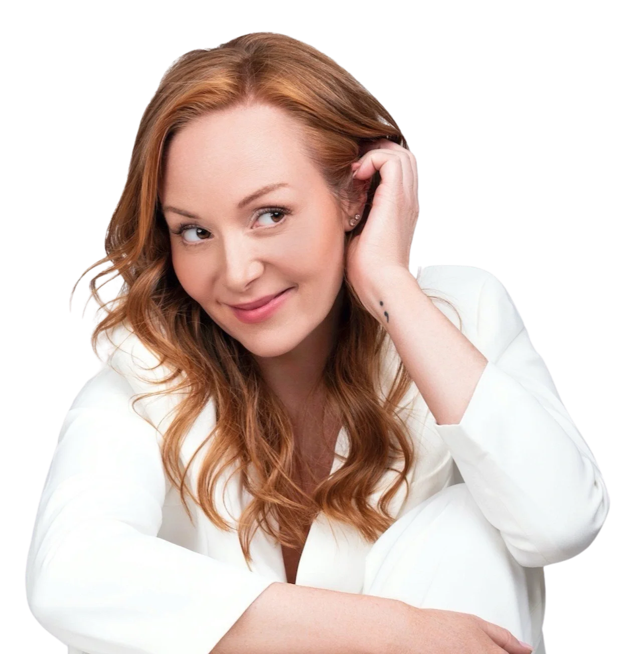 A woman with red hair, smiling and looking to her right, wearing a white blazer with her left hand touching her ear.