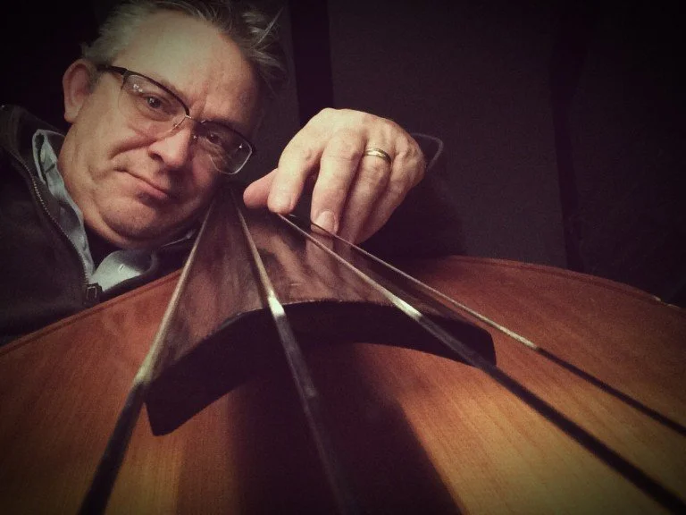 A man with glasses and gray hair adjusting the strings of a guitar viewed from below.