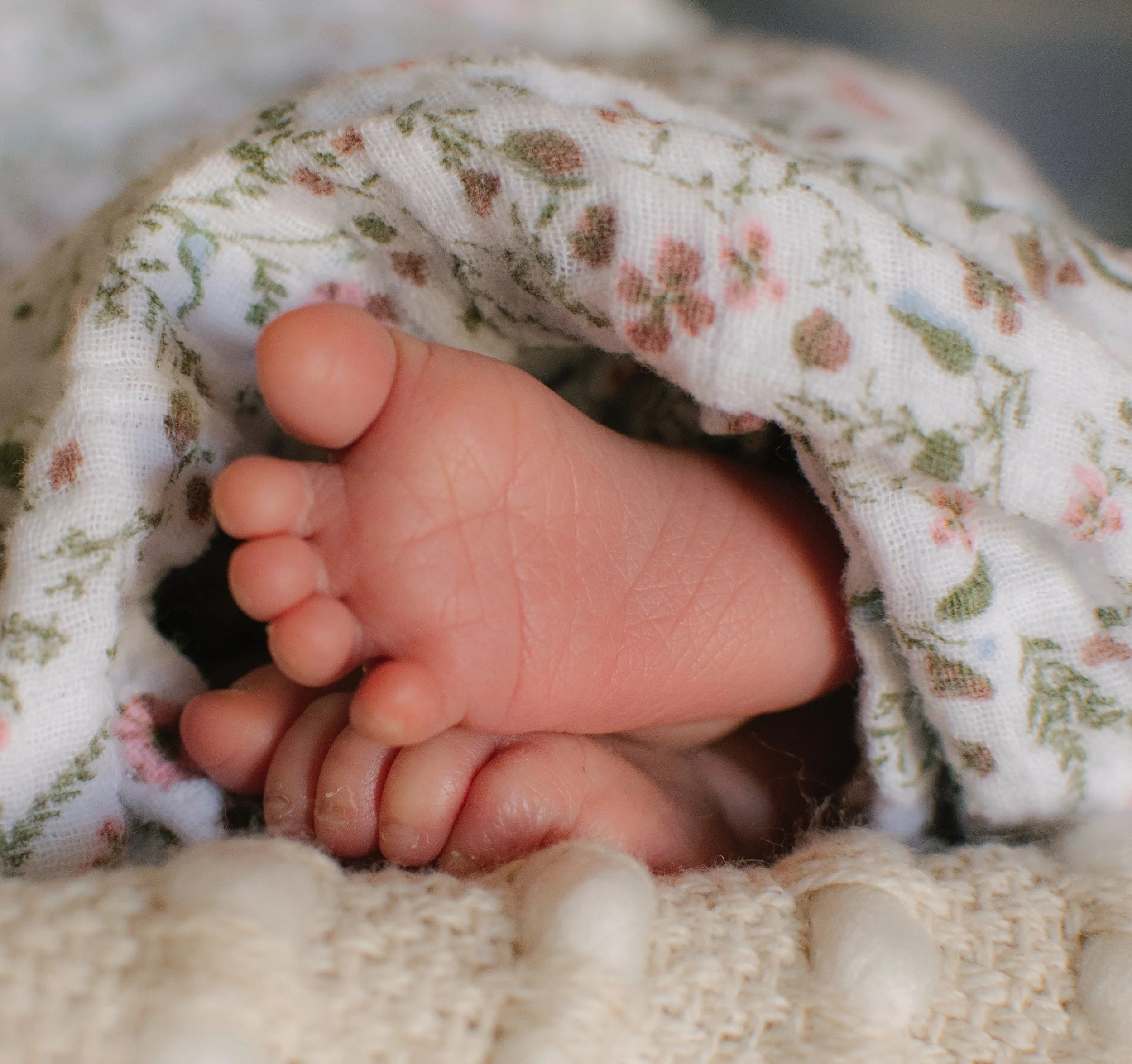 Close-up of a newborn baby's foot wrapped in a floral-patterned cloth, resting on a soft, textured blanket.