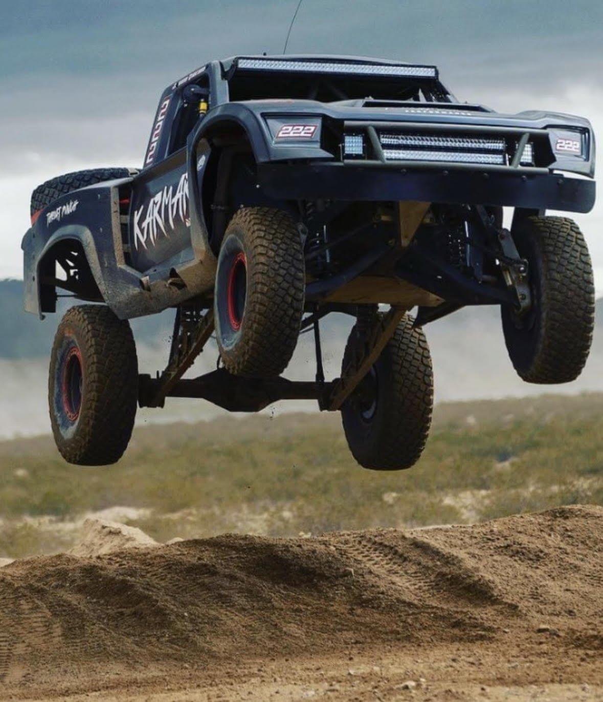 An off-road race truck airborne over dirt tracks during a race event.