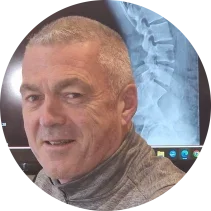 A qualified chiropractor. The headshot includes a portrait of a middle-aged man with short, light hair, wearing a checkered shirt, in an indoor setting.