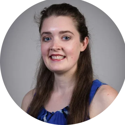 A doctor of chiropractic care. headshot of a young woman with long brown hair, wearing a blue sleeveless top, smiling against a gray background.