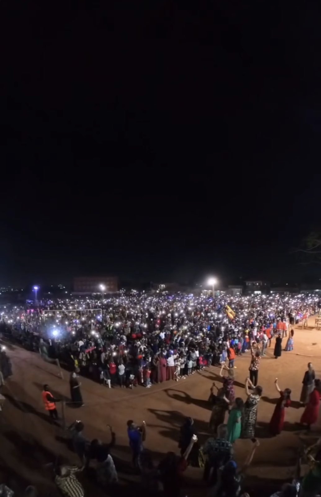 A wide nighttime view of a massive crowd gathered in an open field