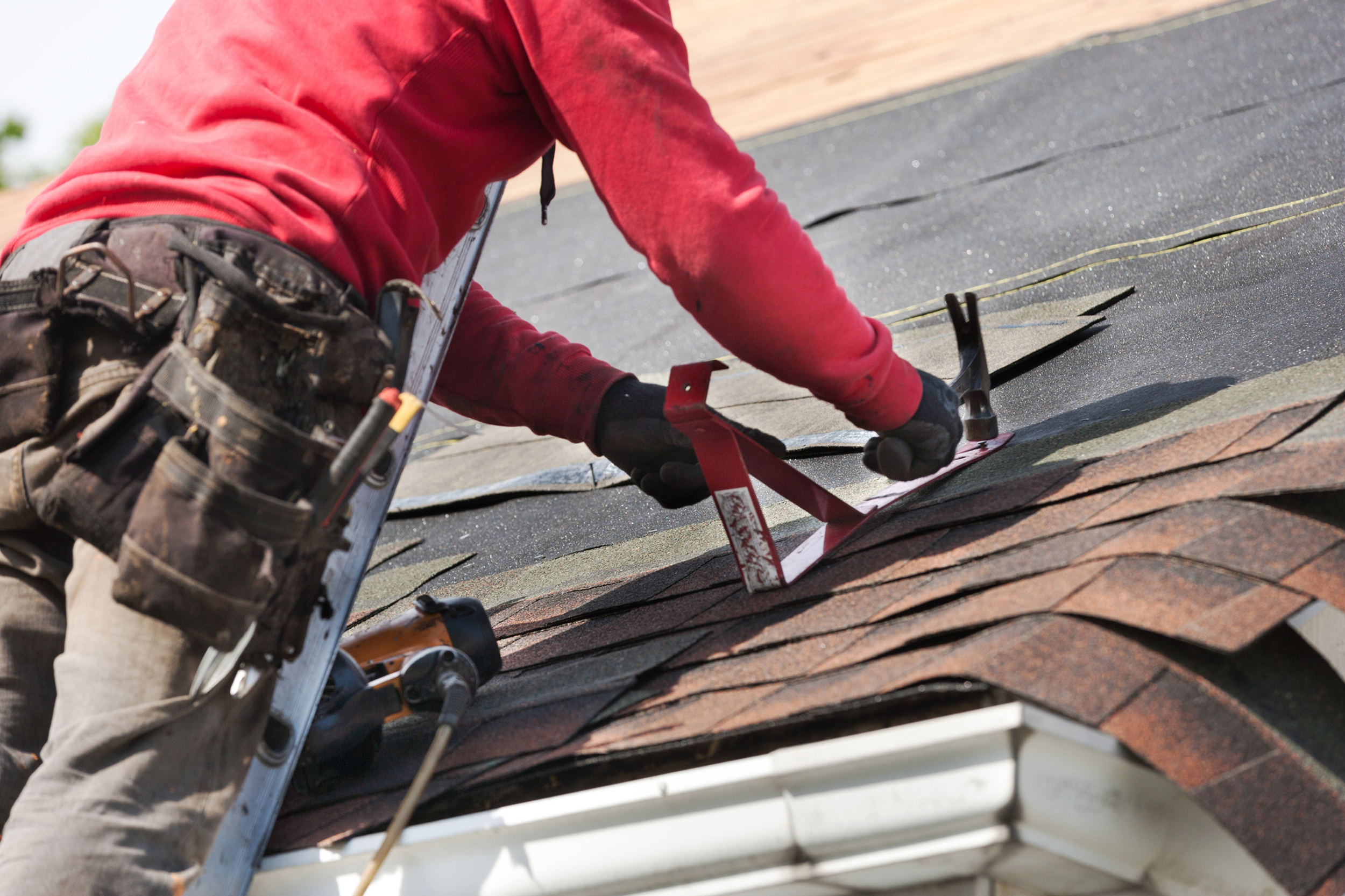 Worker installing or repairing roof shingles with tools on a sloped roof.