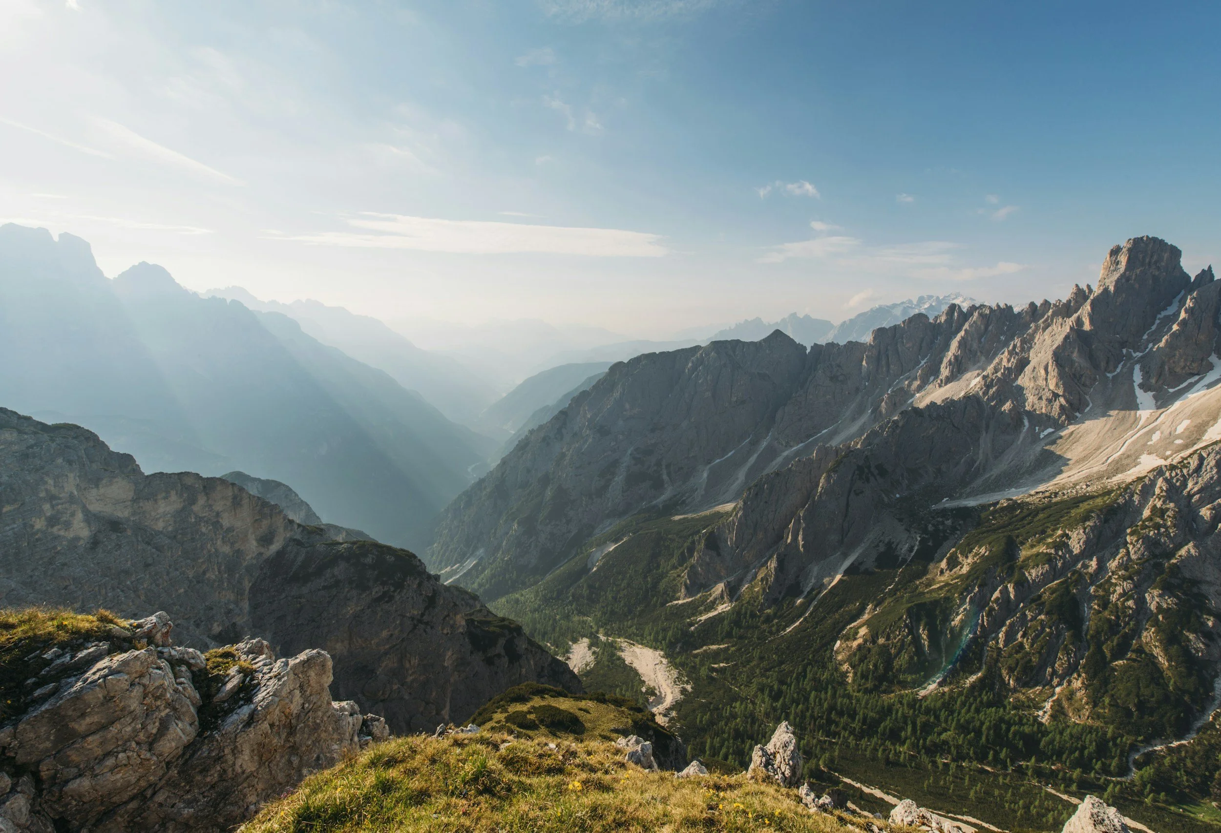 Mountain valley landscape with layered rocky peaks and sunlight in the distance