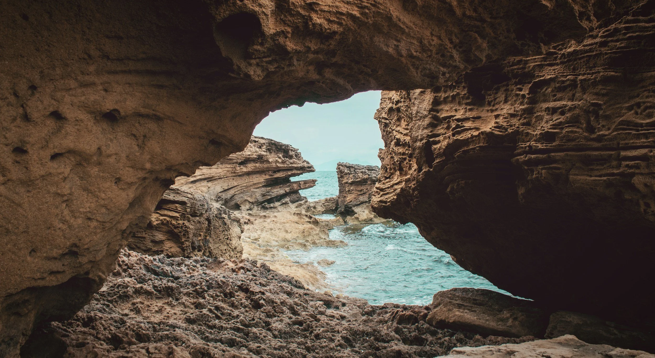 Natural rock arch along a rocky coastline with ocean water beyond