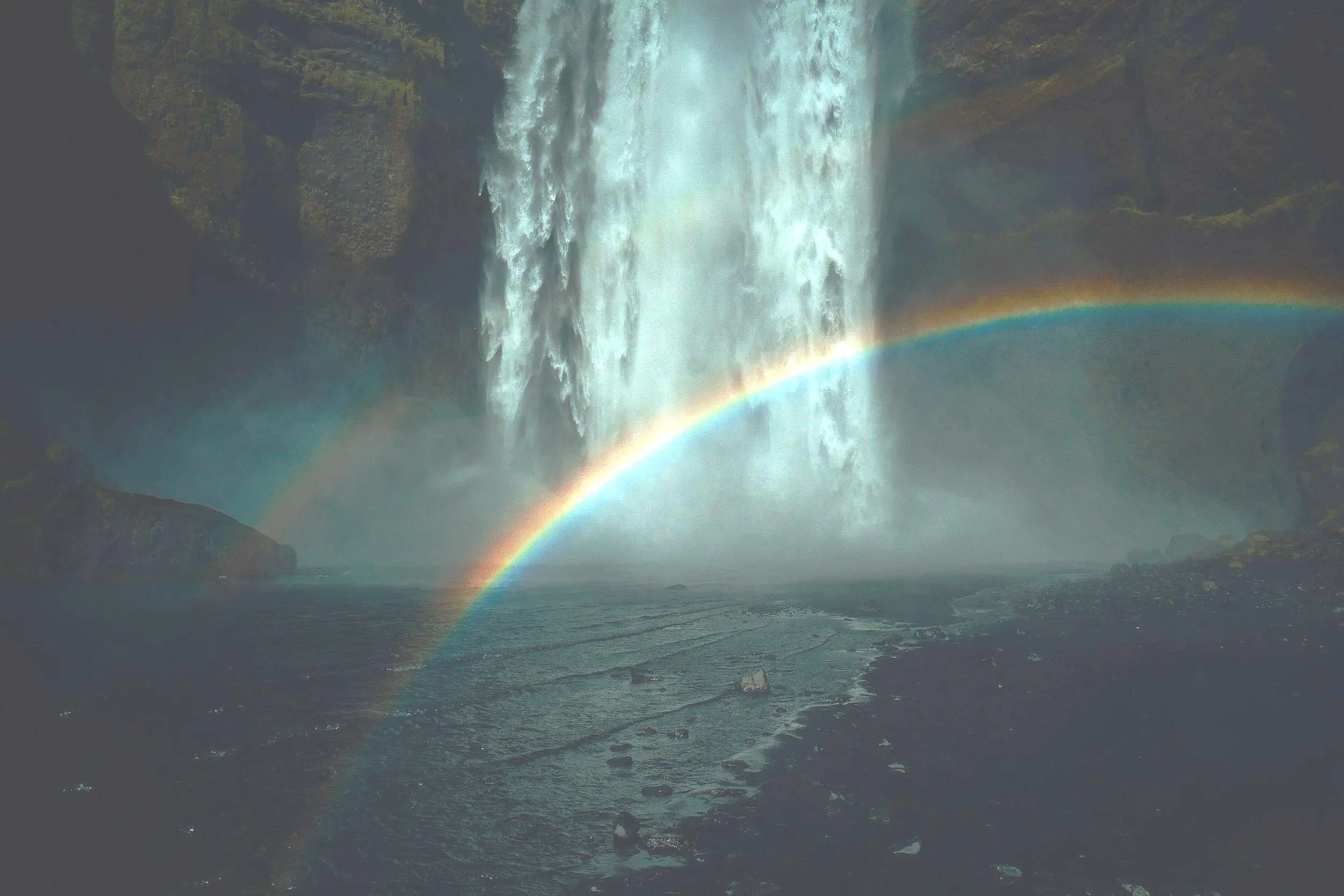 Waterfall cascading into a rocky river with a bright rainbow arching through mist for spiritual awakening