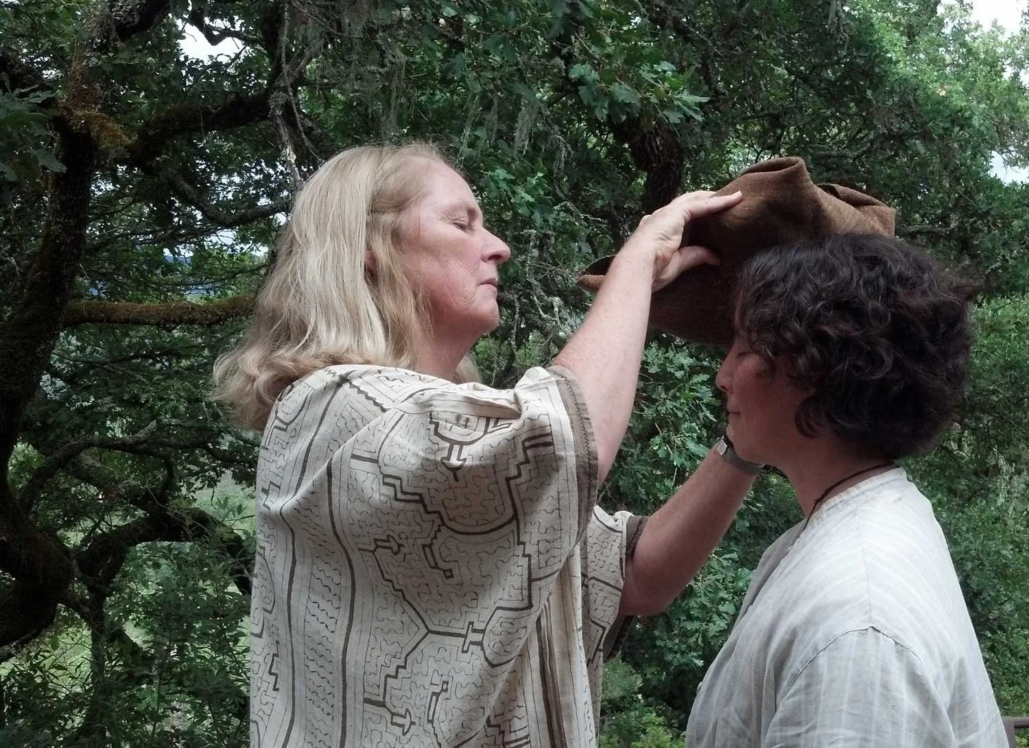 A shamanic woman blesses a young woman by placing a medicine bundle on her head