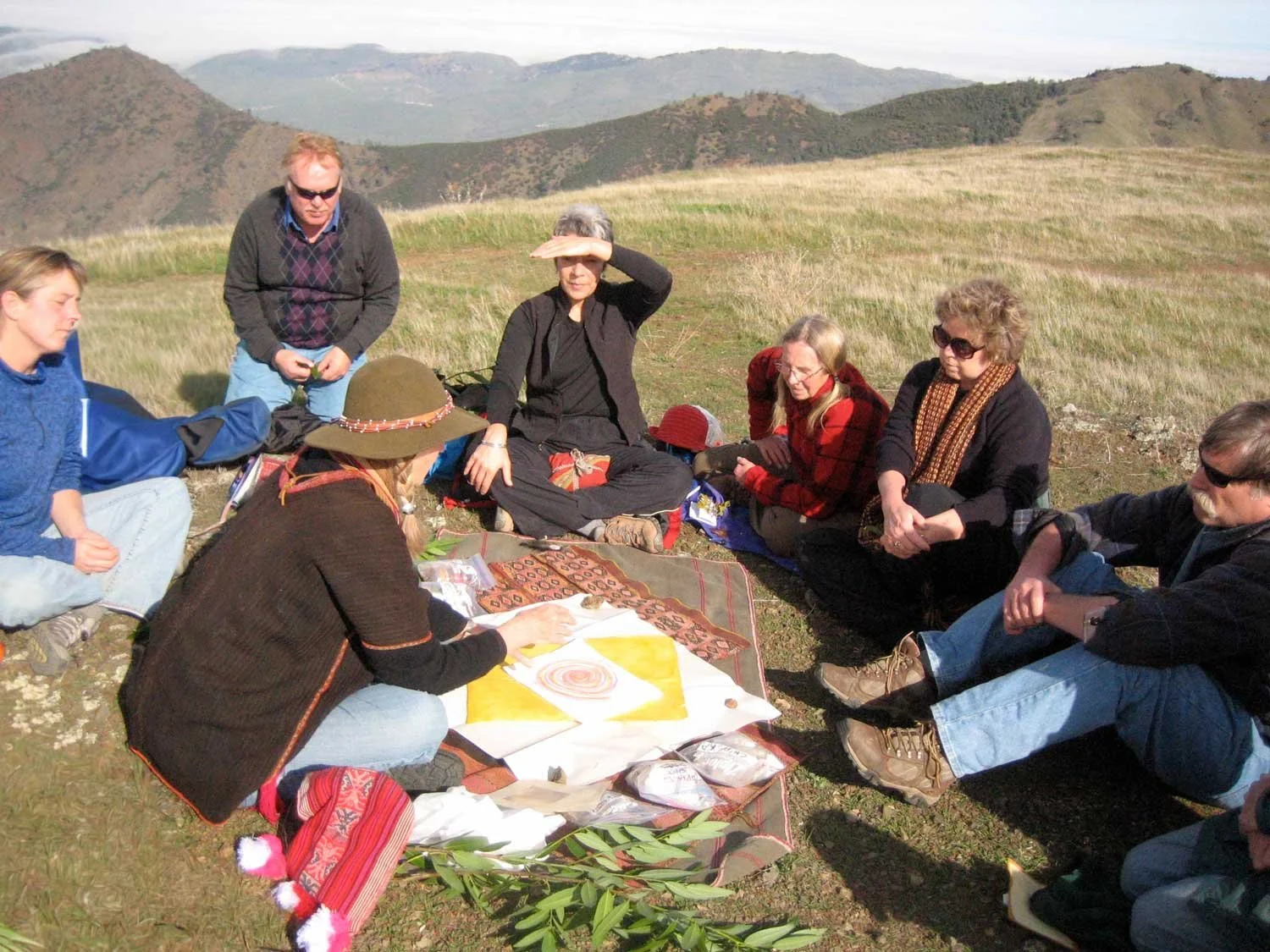 A group sits on the ground in nature as they perform a healing ritual with sacred objects and symbols