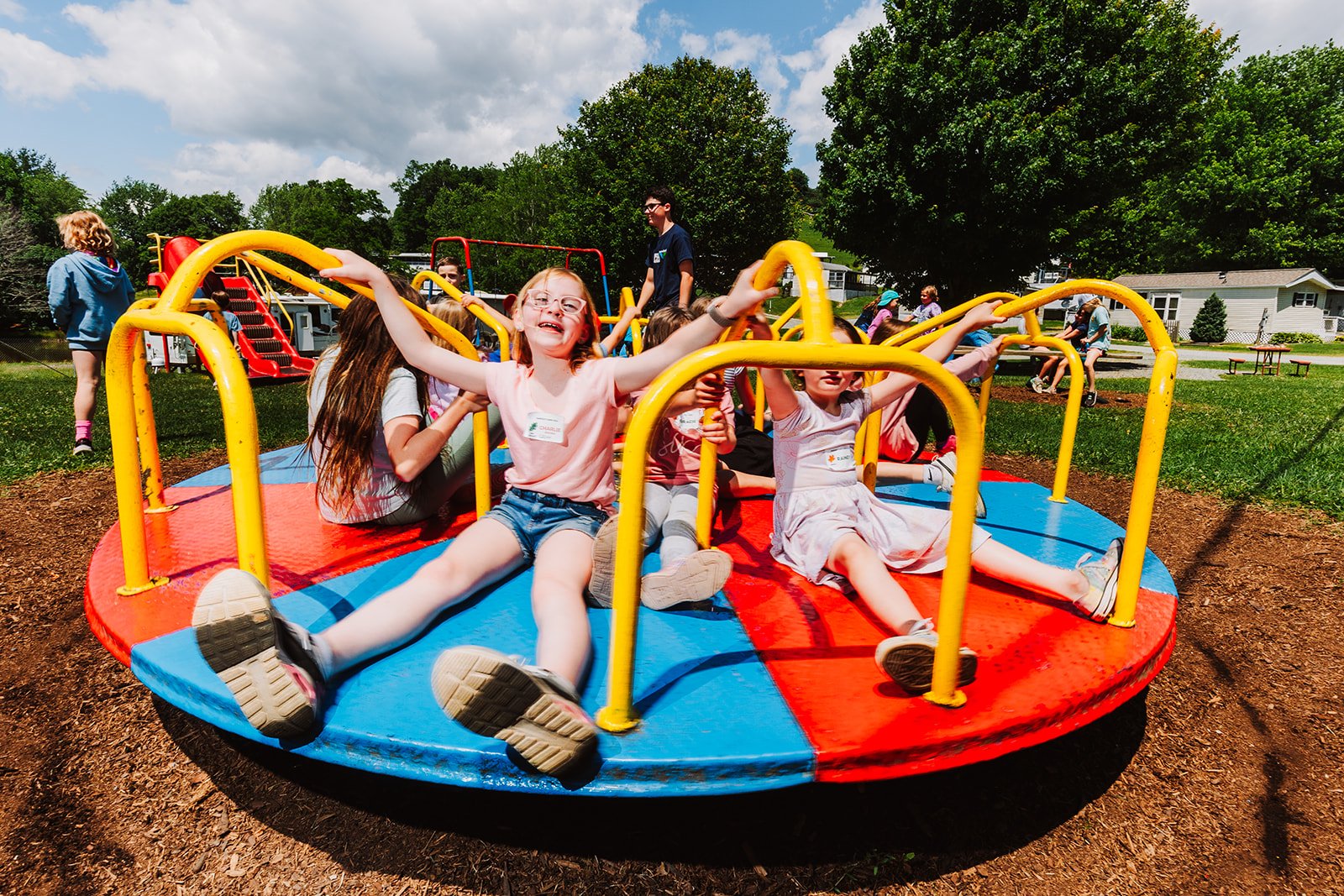 Children playing on a colorful merry-go-round at a playground on a sunny day.