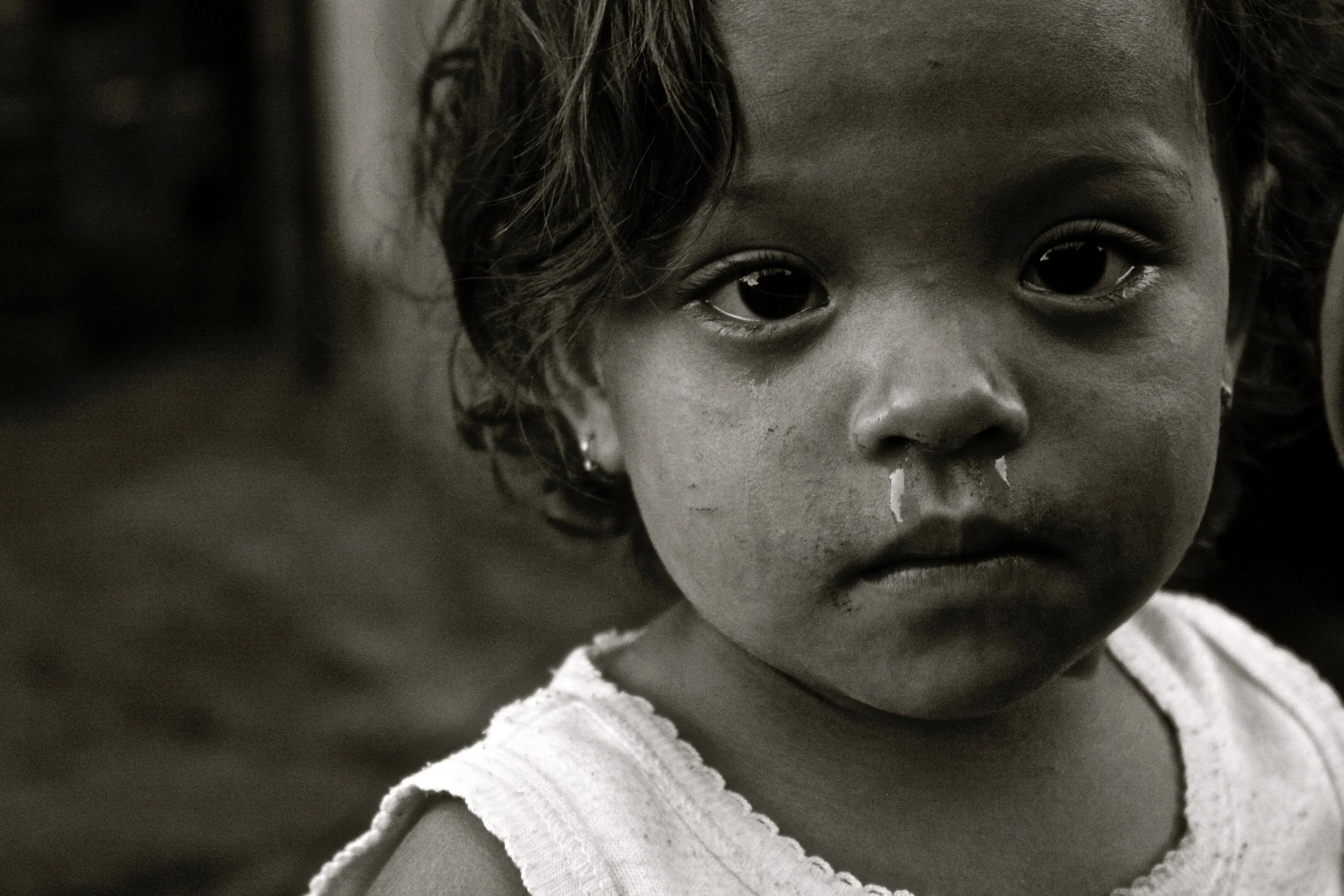 A young girl with dark hair and earrings, looking directly into the camera with a serious expression, in black and white.