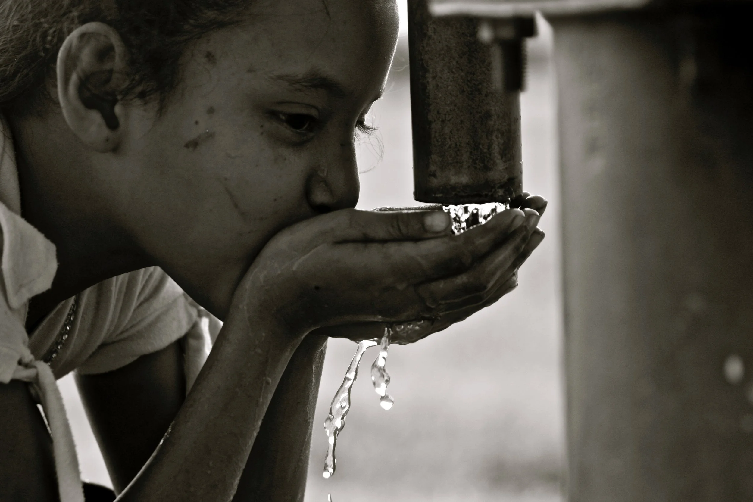 A young girl drinking water from a pipe with water flowing out.