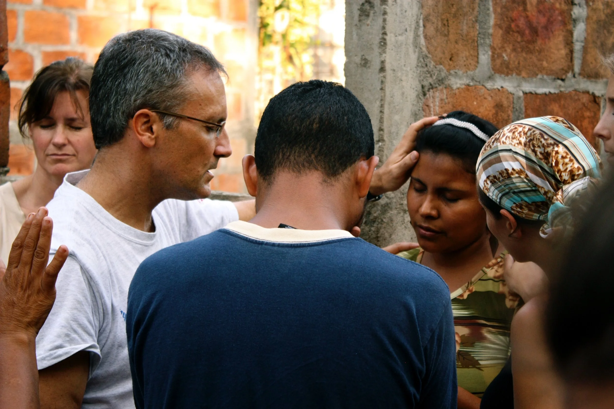 Group of people praying together with heads bowed and hands on each other's shoulders.