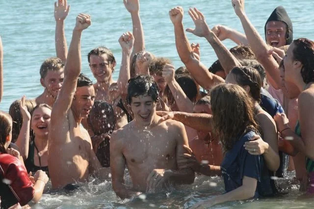 Group of young people having fun and splashing in the water at a beach, celebrating and smiling.