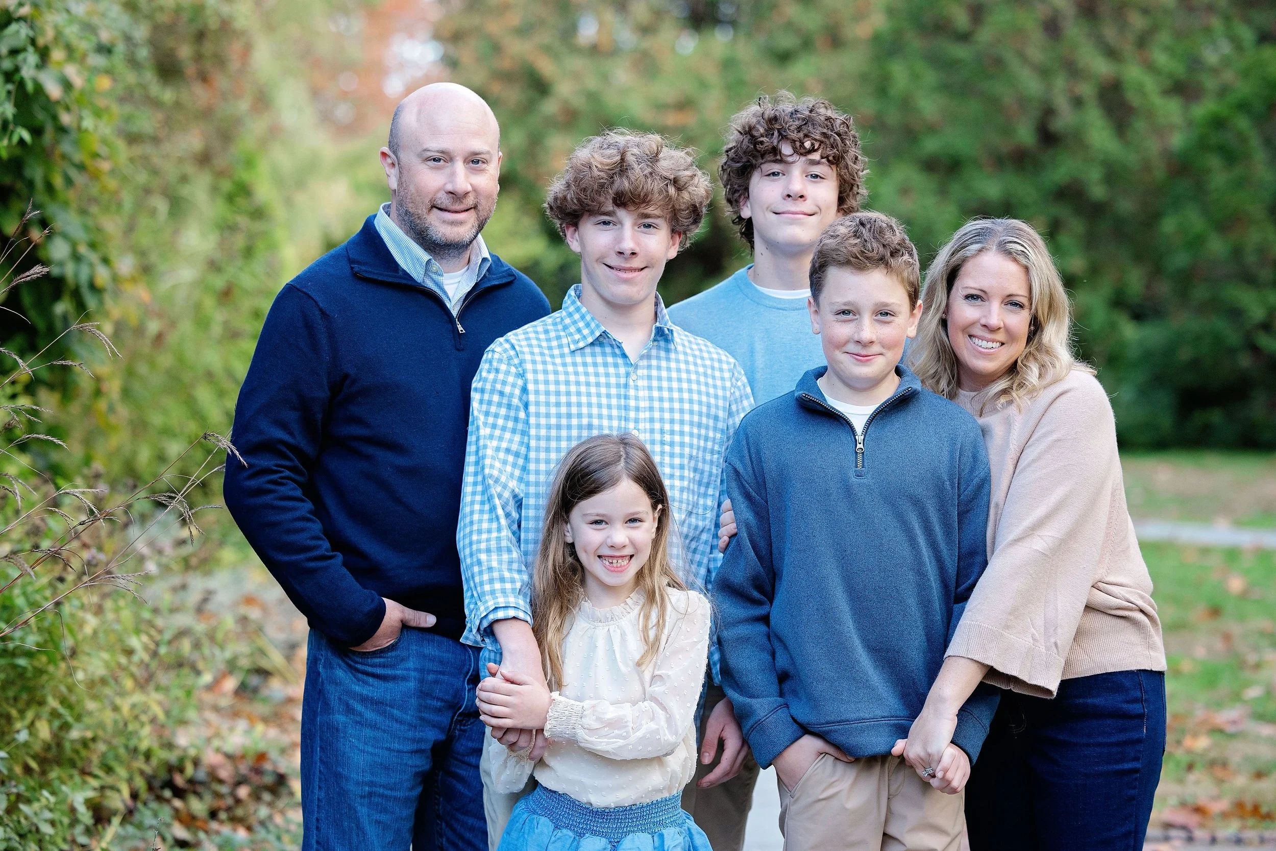A family of seven standing outdoors in a natural setting, smiling at the camera, dressed casually.