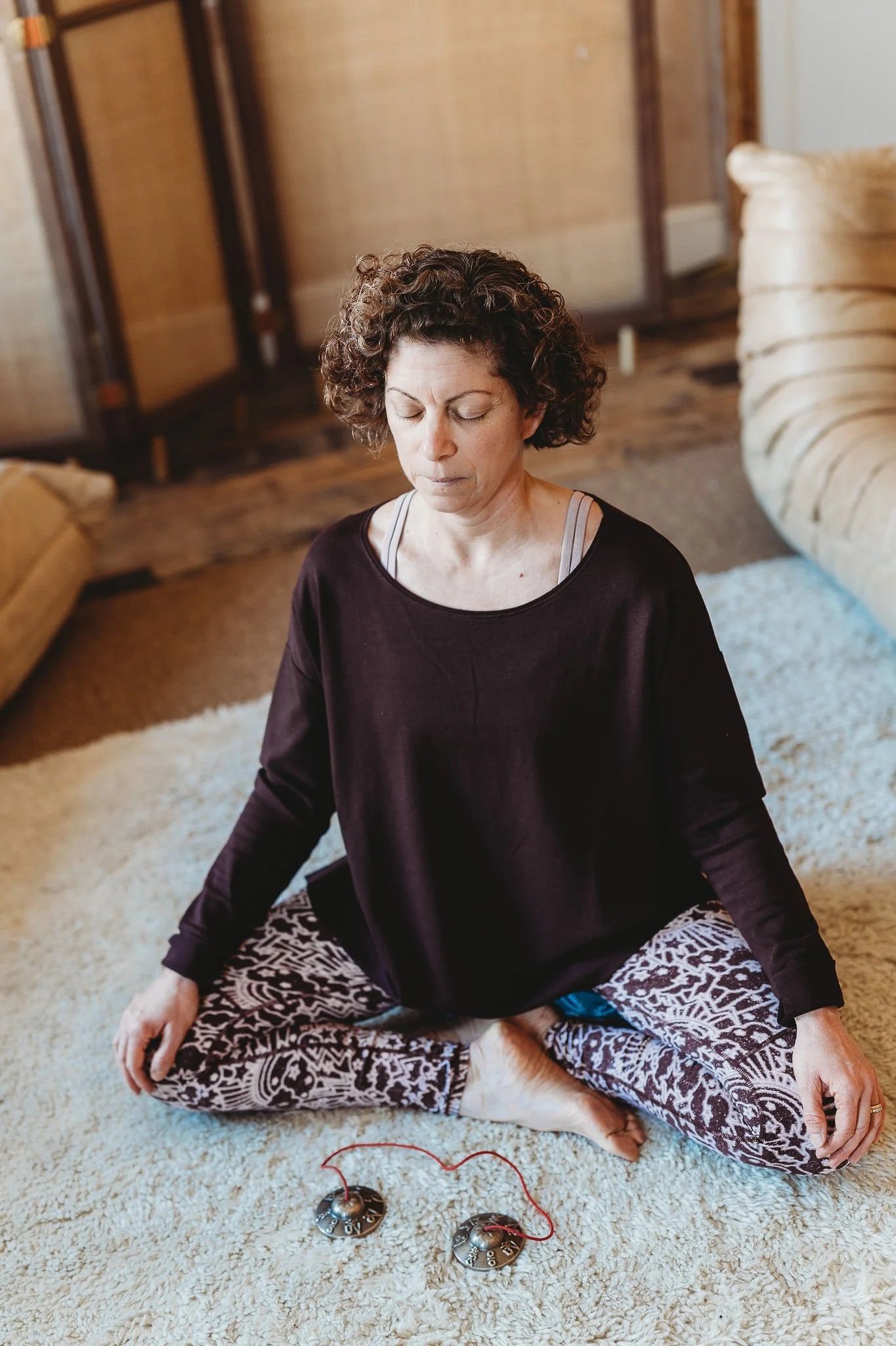 Zeina Charara, meditation guide, practicing mindfulness meditation. She is sitting cross-legged with her eyes closed, and there are two singing bowls with red cords in front of her.