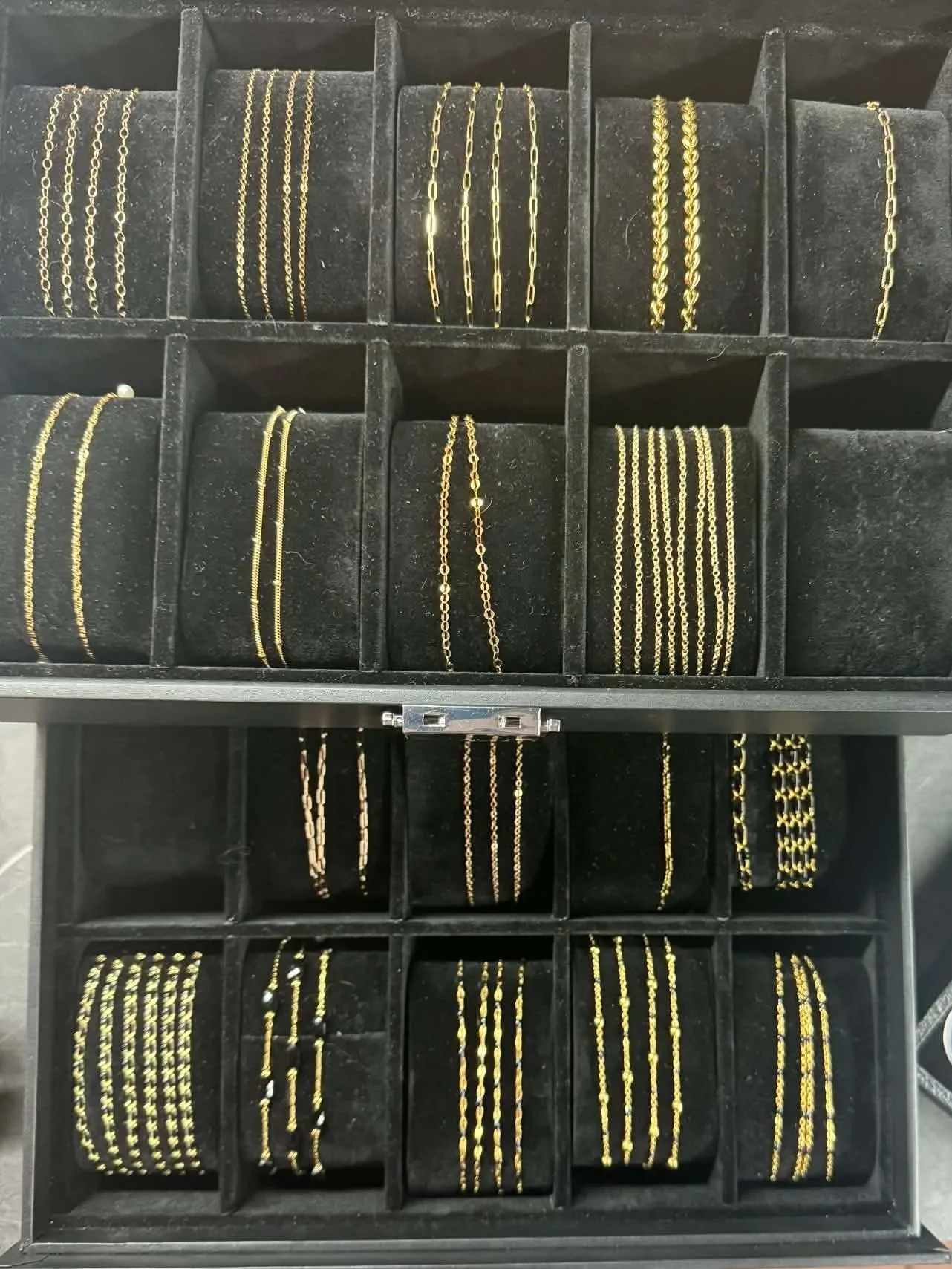A black jewelry box divided into compartments, each containing gold necklaces with various chain designs.