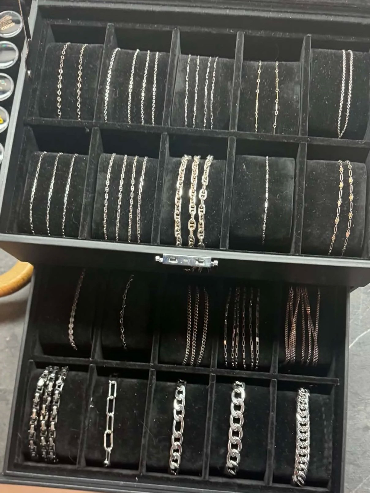 A jewelry box containing various silver and gold chains and necklaces arranged in compartments.