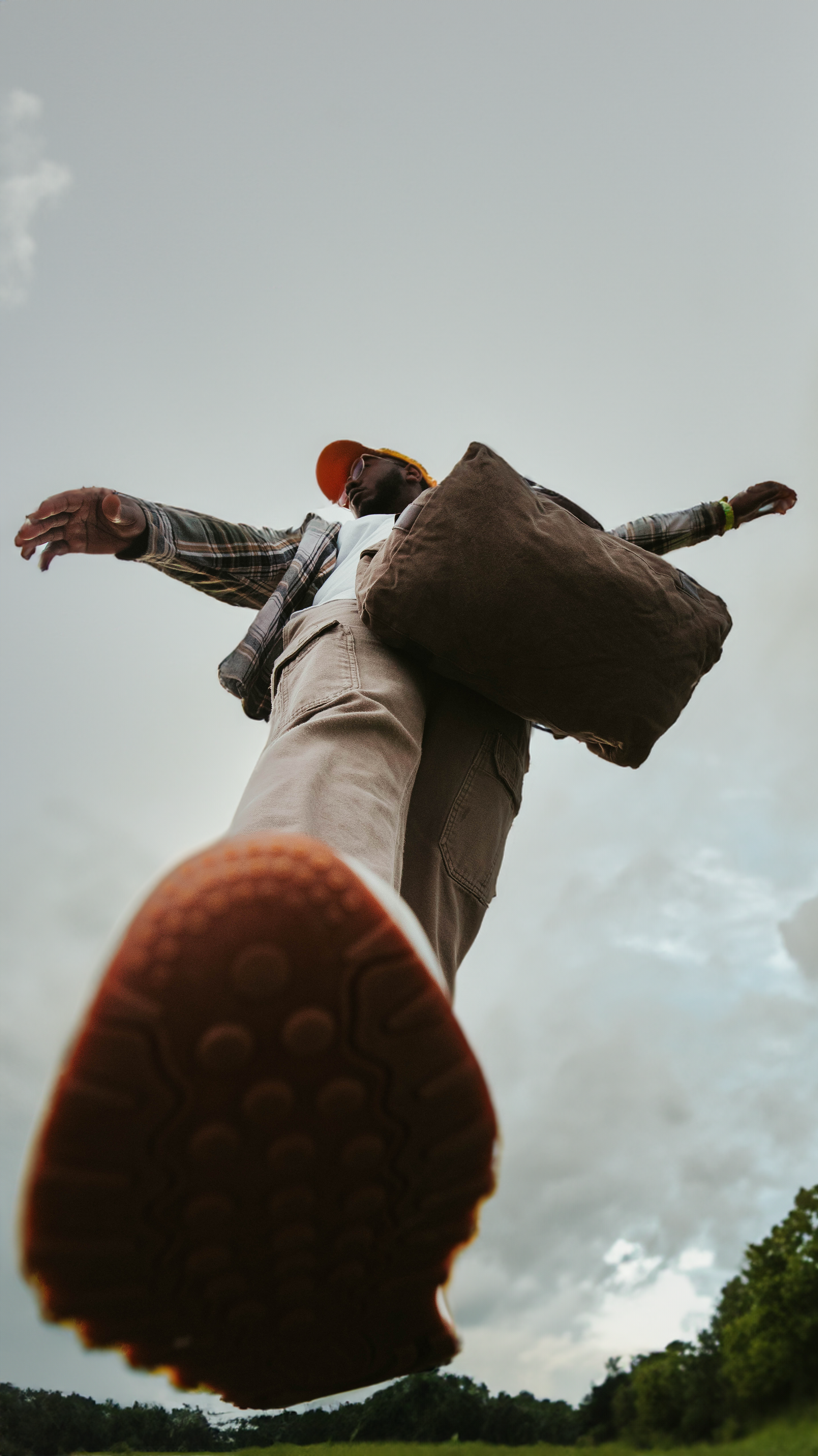 low angle portrait with a focus on the shoe, a man stands over the camera with his arms outstretched looking to the left