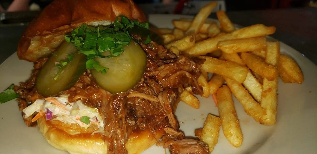 An absolutely delicious, pulled pork sandwich with homemade coleslaw, pickles, and cilantro on a toasted bun with a large side order of fries at the Waterworks restaurant in Rockland, Maine