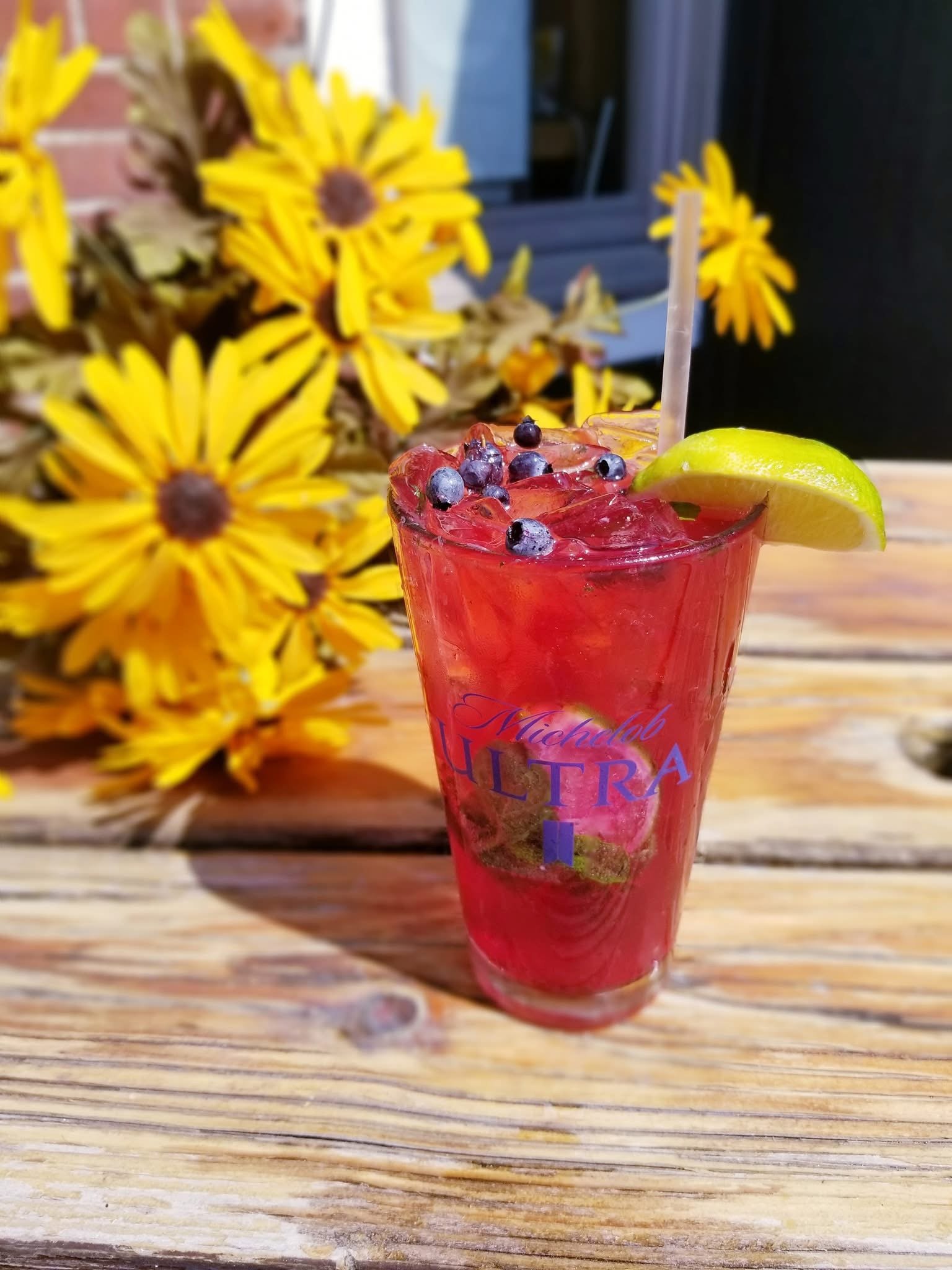 A refreshing classic cocktail with a fresh main blueberry topper on our amazing spacious patio with gorgeous flowers in the background at Waterworks restaurant in Rockland, Maine